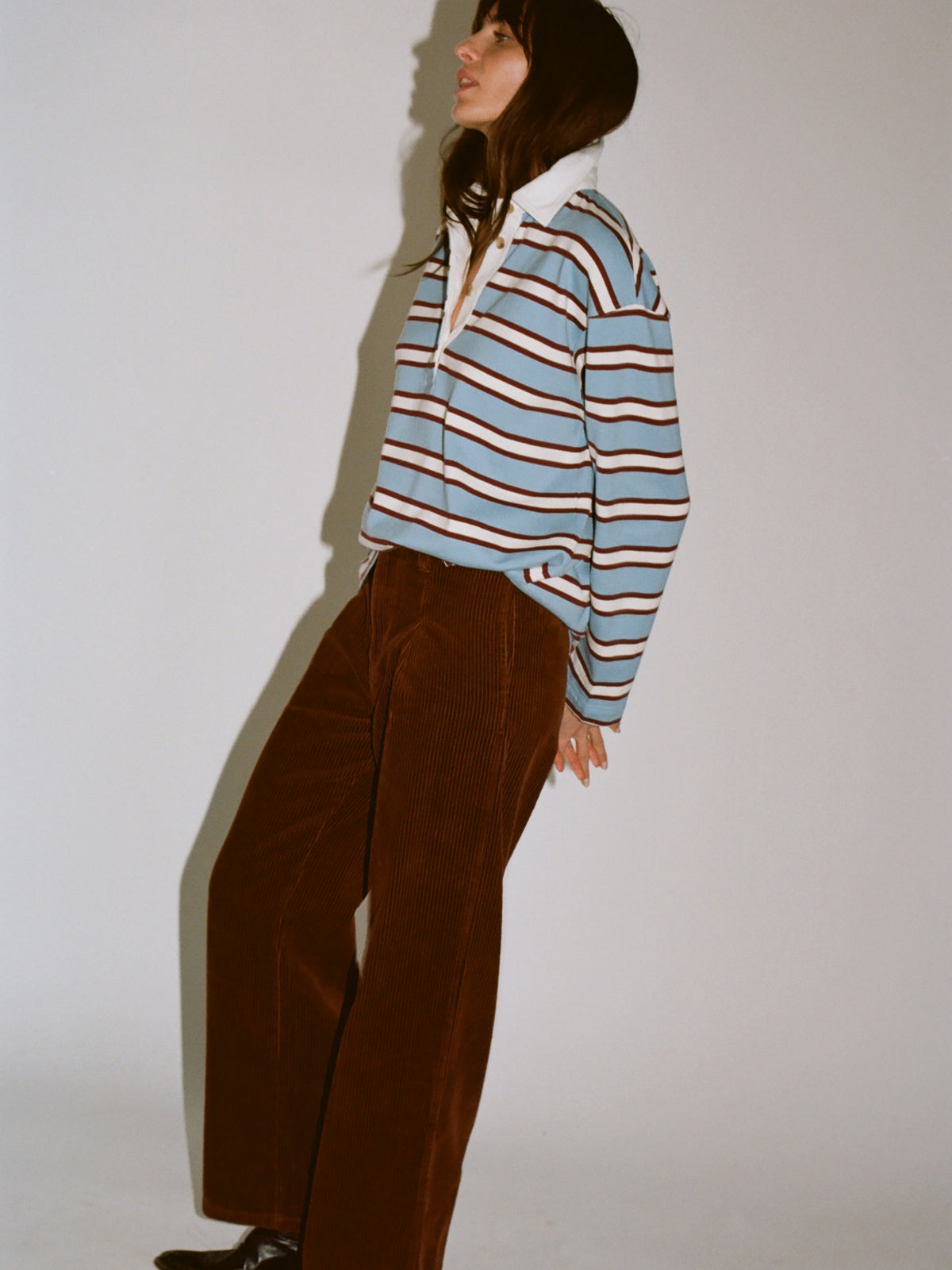 A model wearing a light blue, brown, and white striped rugby shirt paired with brown corduroy trousers, image 2 of 7