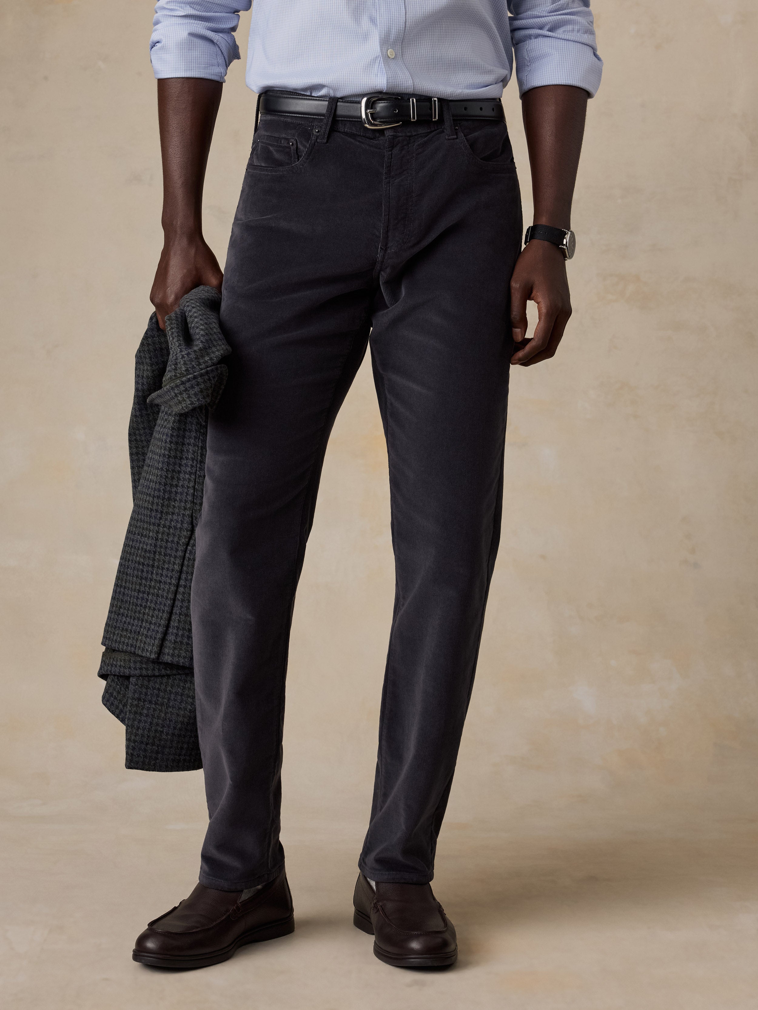 A man wearing a blue button up shirt and grey corduroy pants