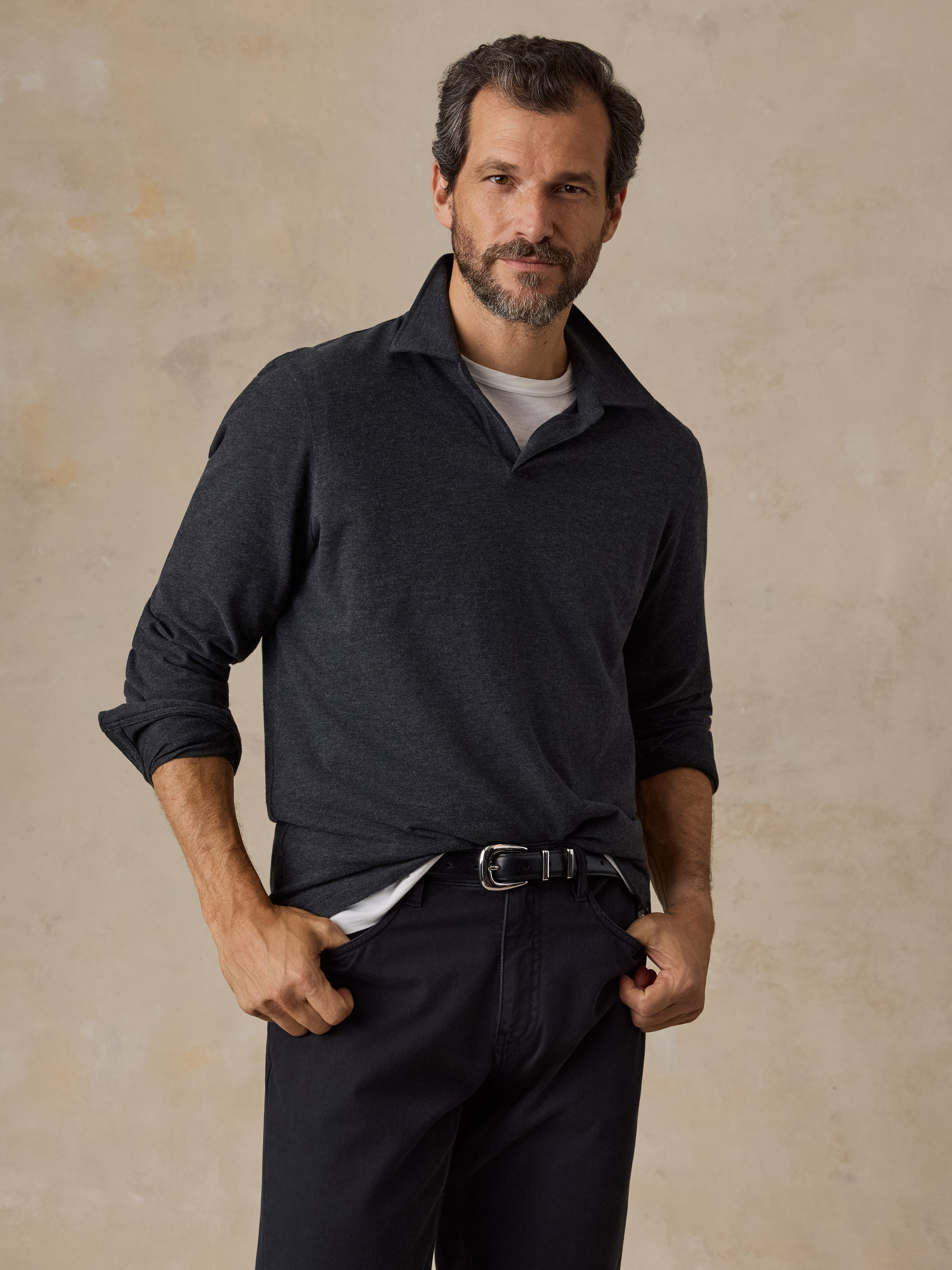 A man wearing a dark grey sweater polo and black chino pants