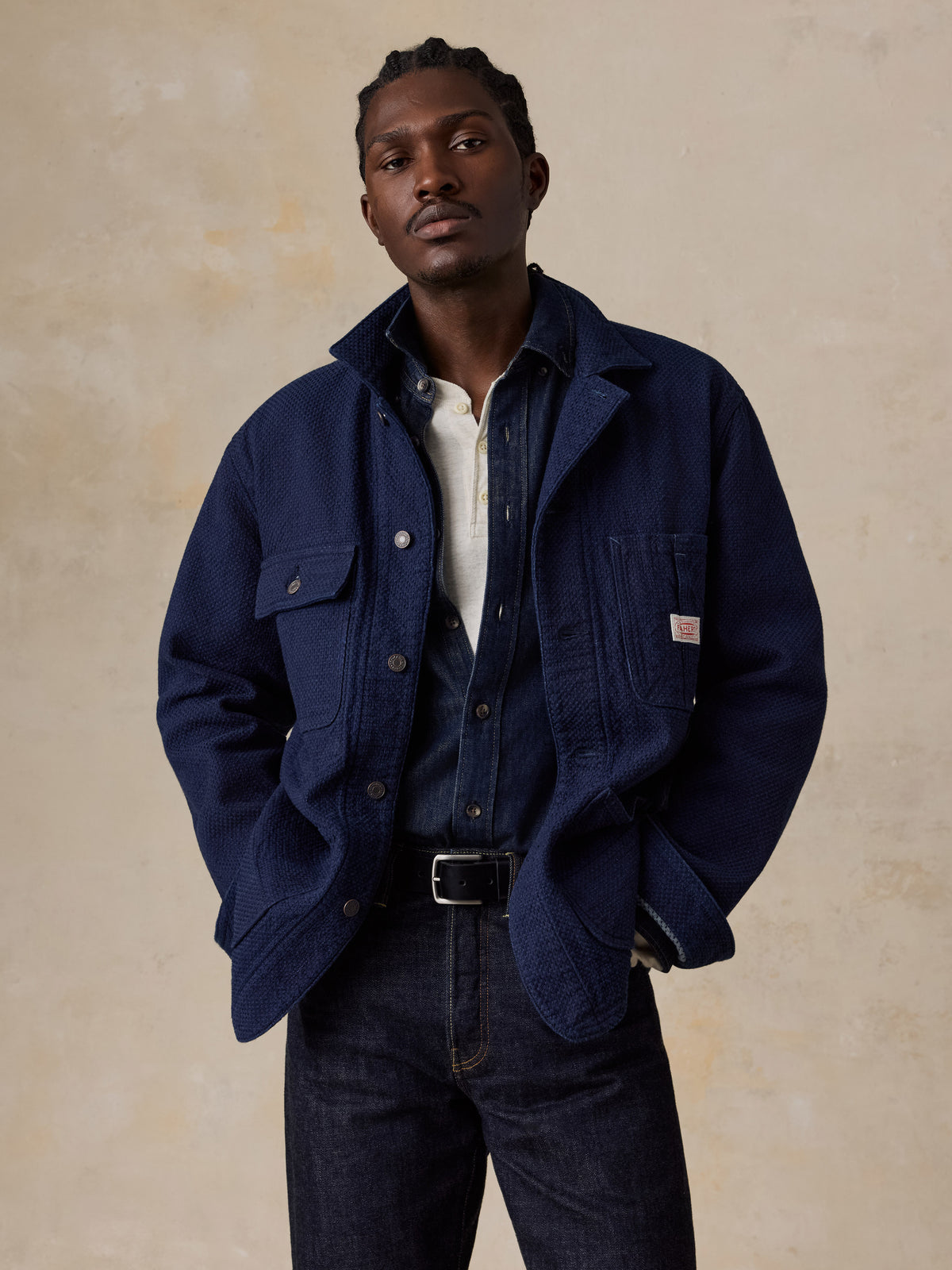 A man wearing a blue jacket over a denim shirt and blue jeans, image 1 of 6