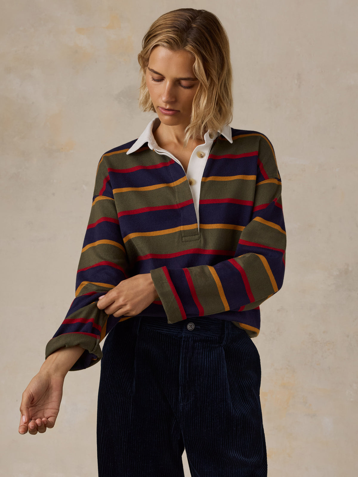 A woman wearing a long-sleeve rugby-style shirt with stripes in olive green, navy blue, red, and mustard yellow , image 1 of 7