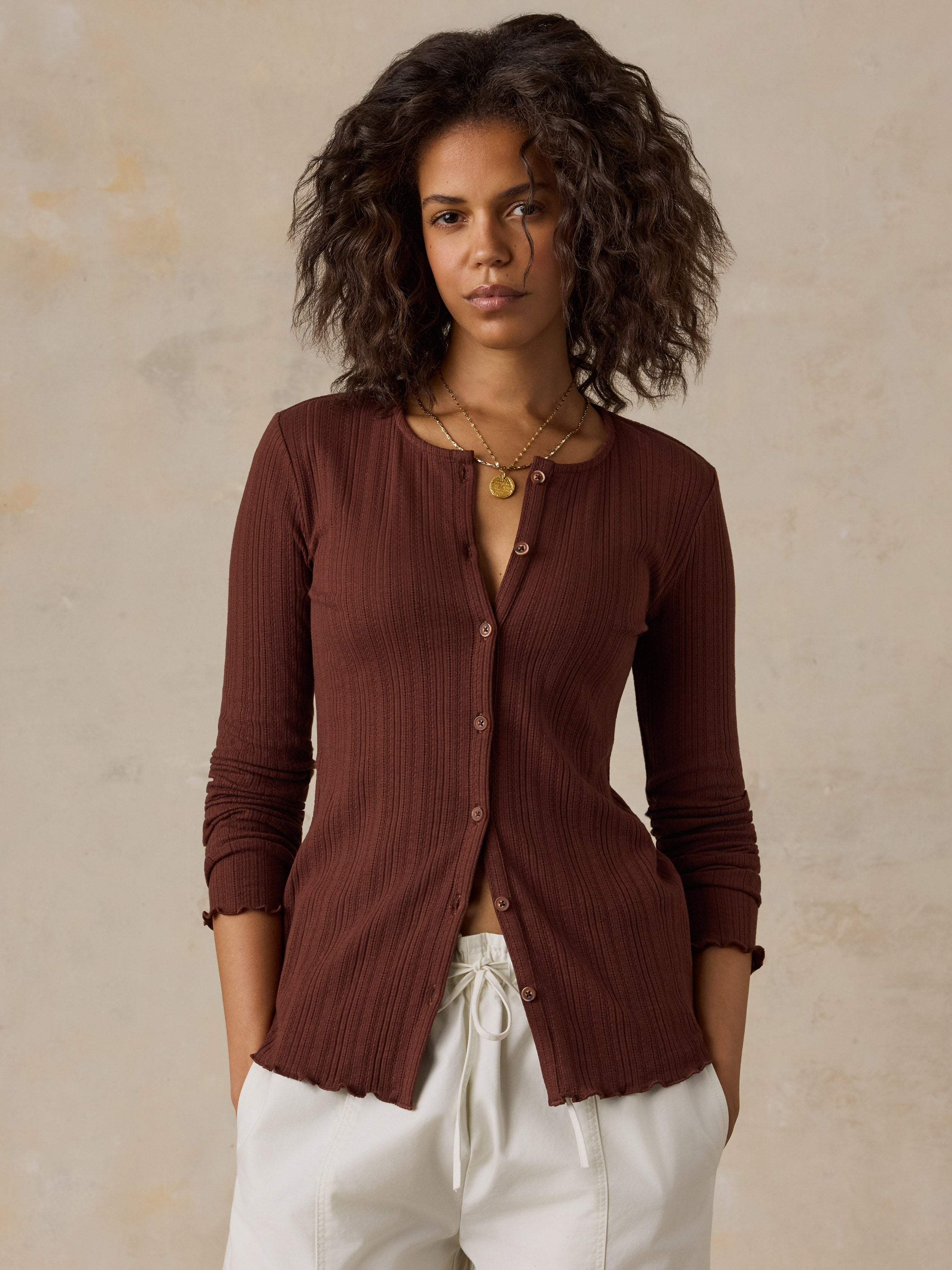 A woman wearing a brown knit cardigan and white pants