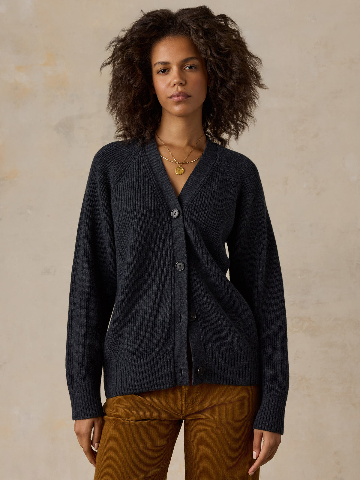 A woman with curly dark hair wearing a dark navy ribbed cardigan and brown pants, image 1 of 6