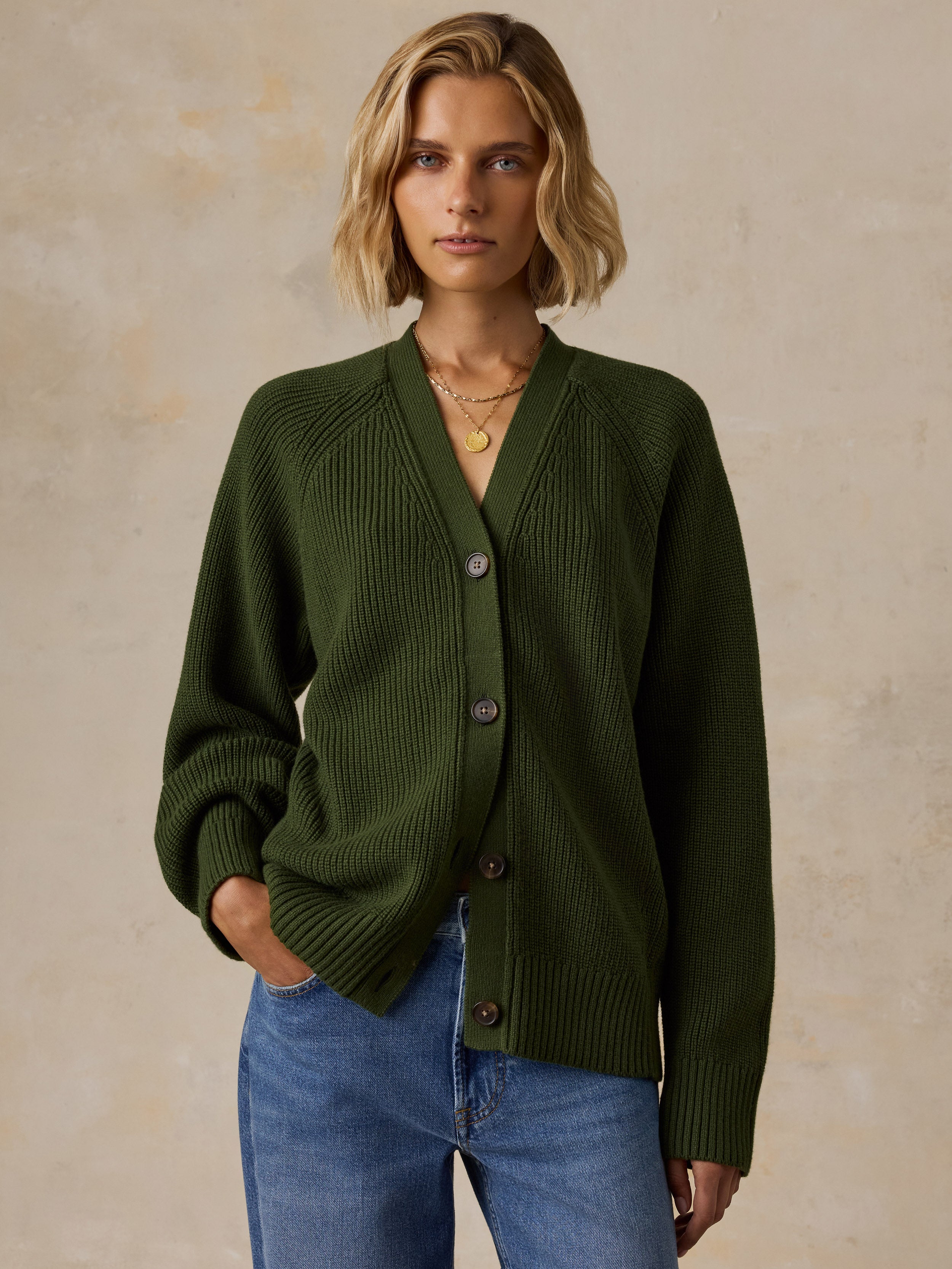 A woman wearing an olive green ribbed knit cardigan with brown buttons, paired with blue jeans