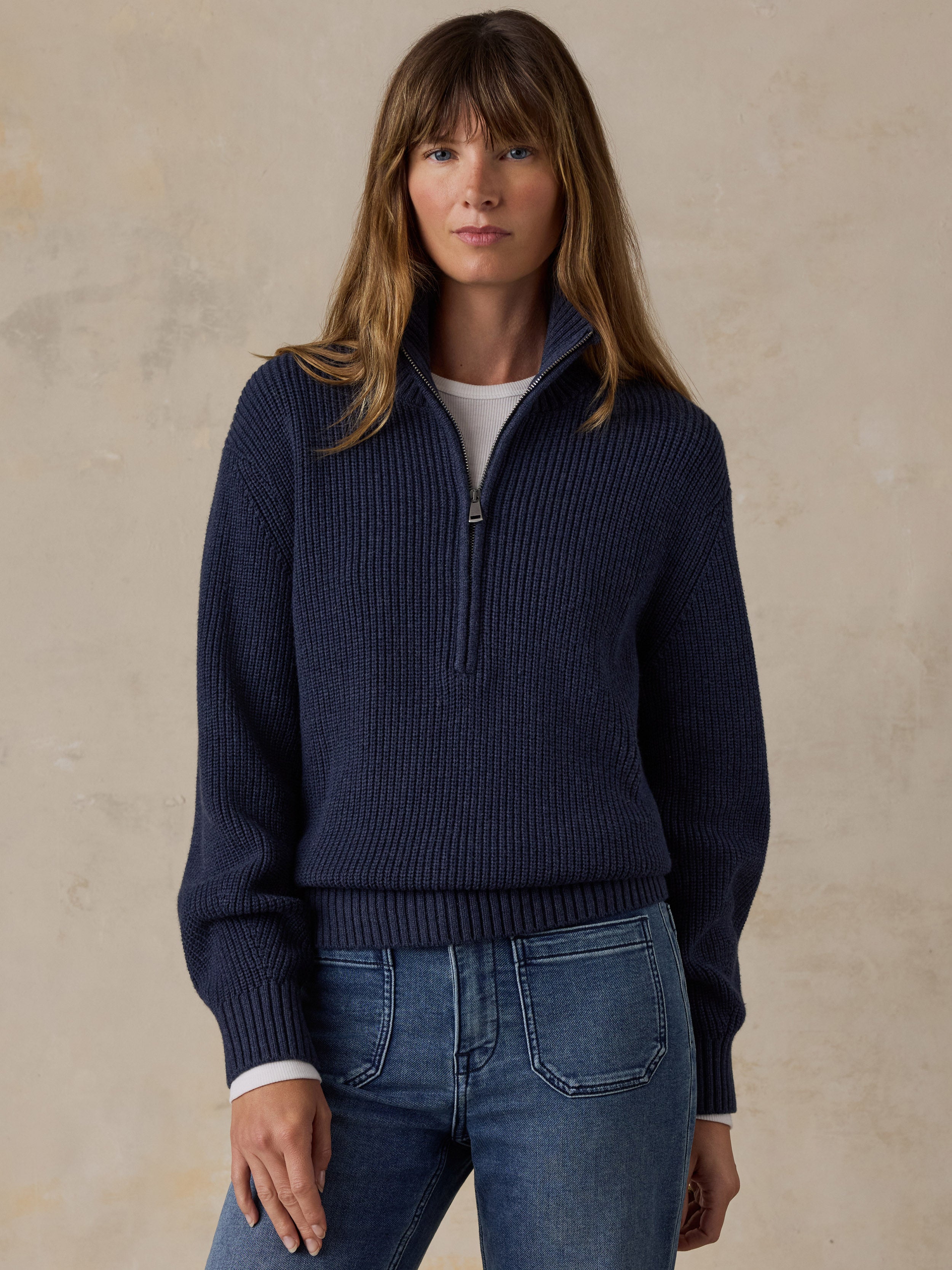Woman wearing a navy blue quarter zip sweater and blue jeans