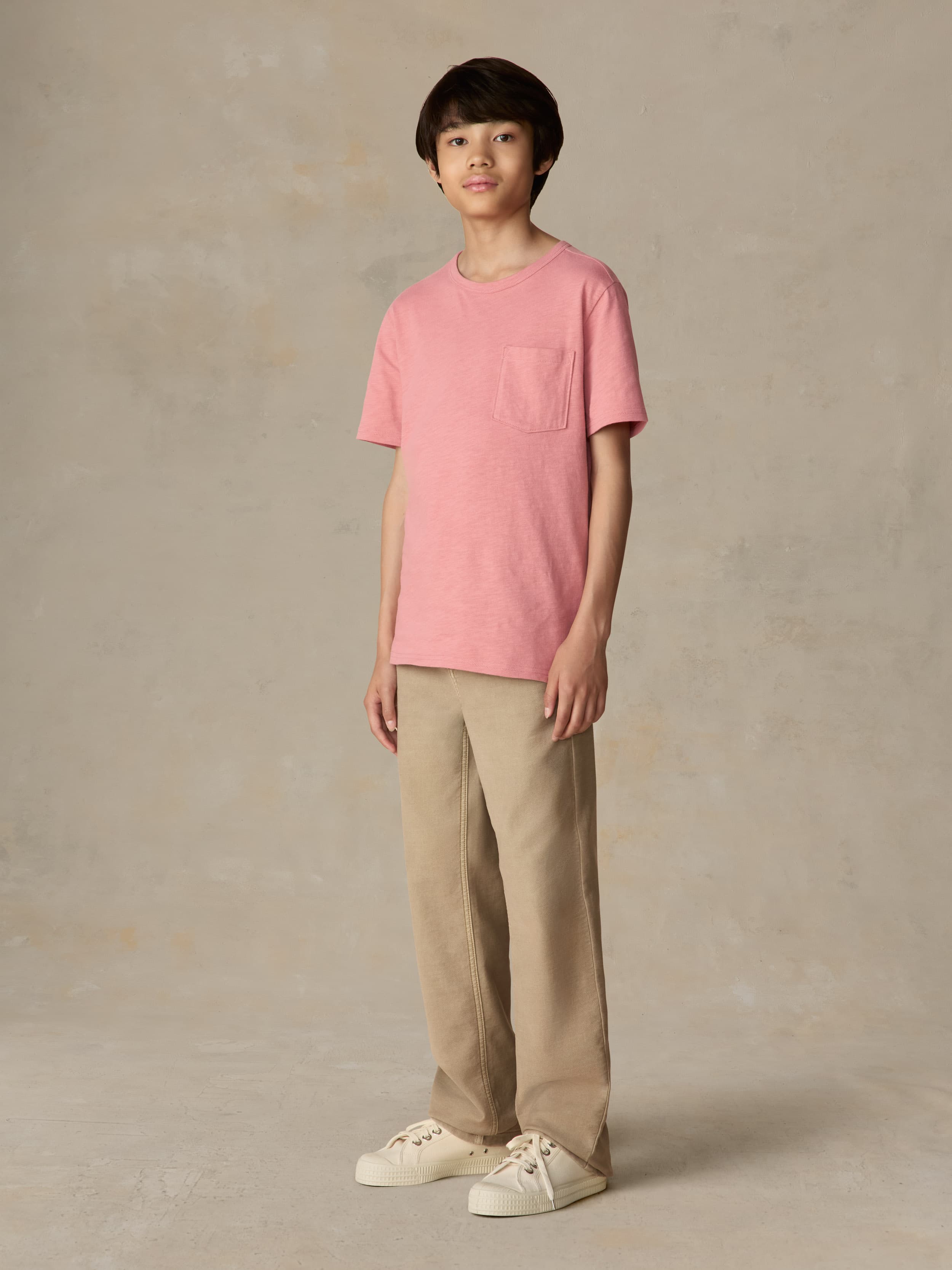 Child wearing a red pocket tee and beige pants against a beige background