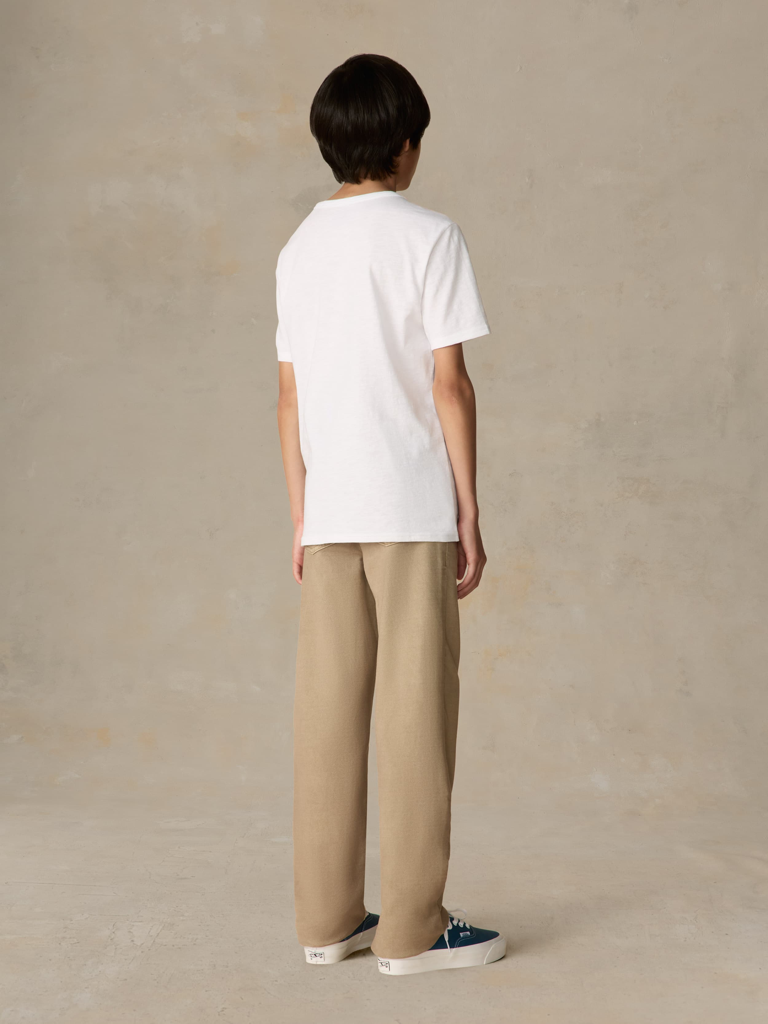 Child wearing a white shirt and beige pants against a beige background