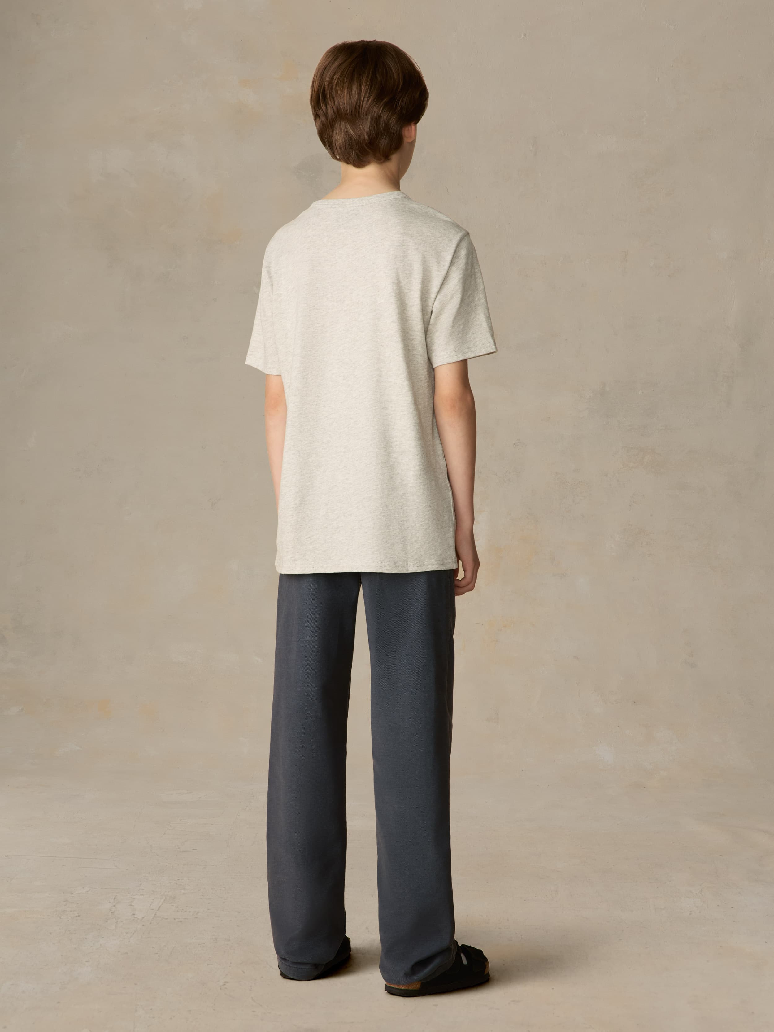 Child wearing a grey surf & ski club tee and black pants against a beige background