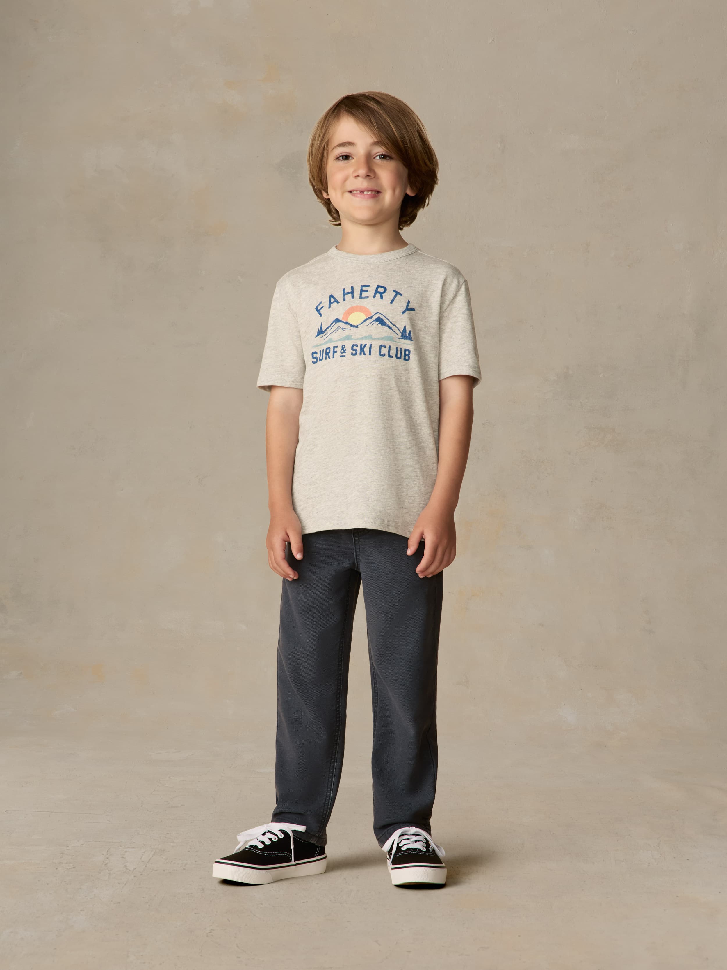 Child wearing a grey surf & ski club tee and black pants against a beige background