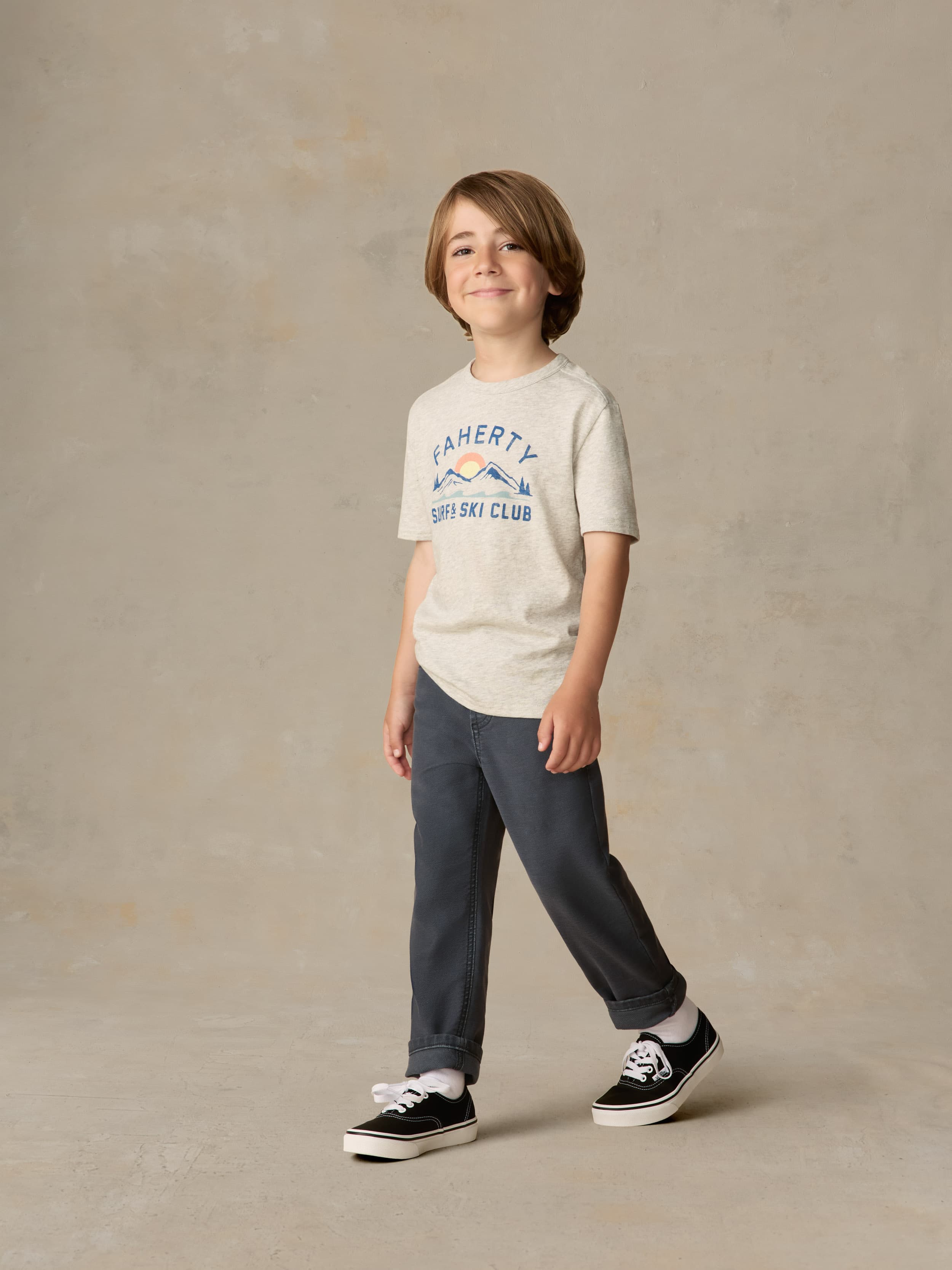 Child wearing a grey surf & ski club tee and black pants against a beige background