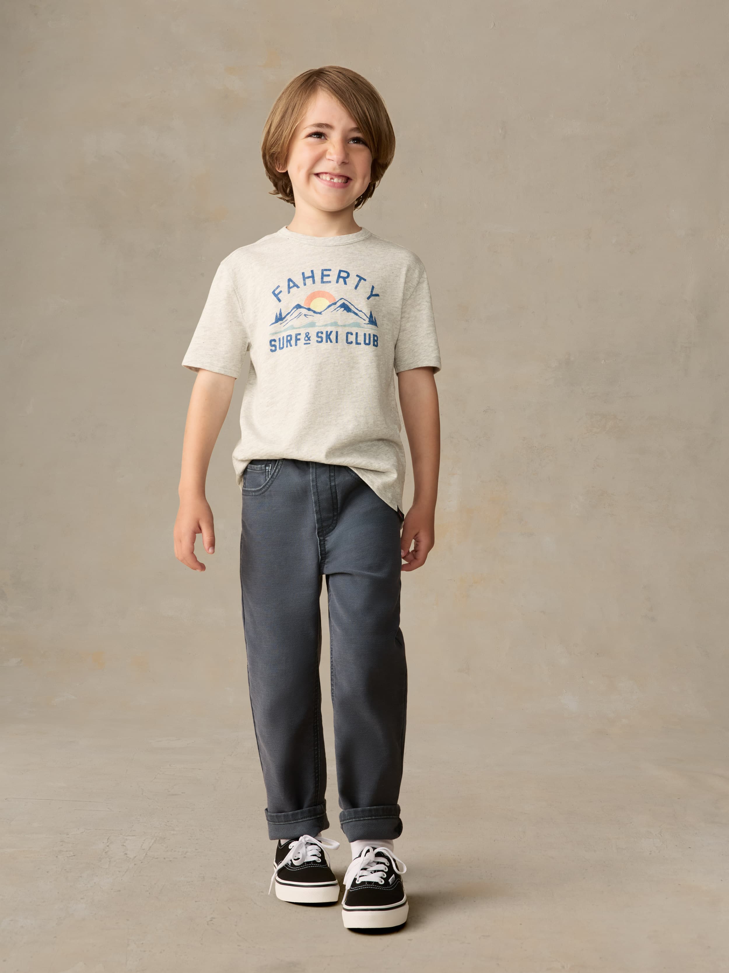 Child wearing a grey surf & ski club tee and black pants against a beige background