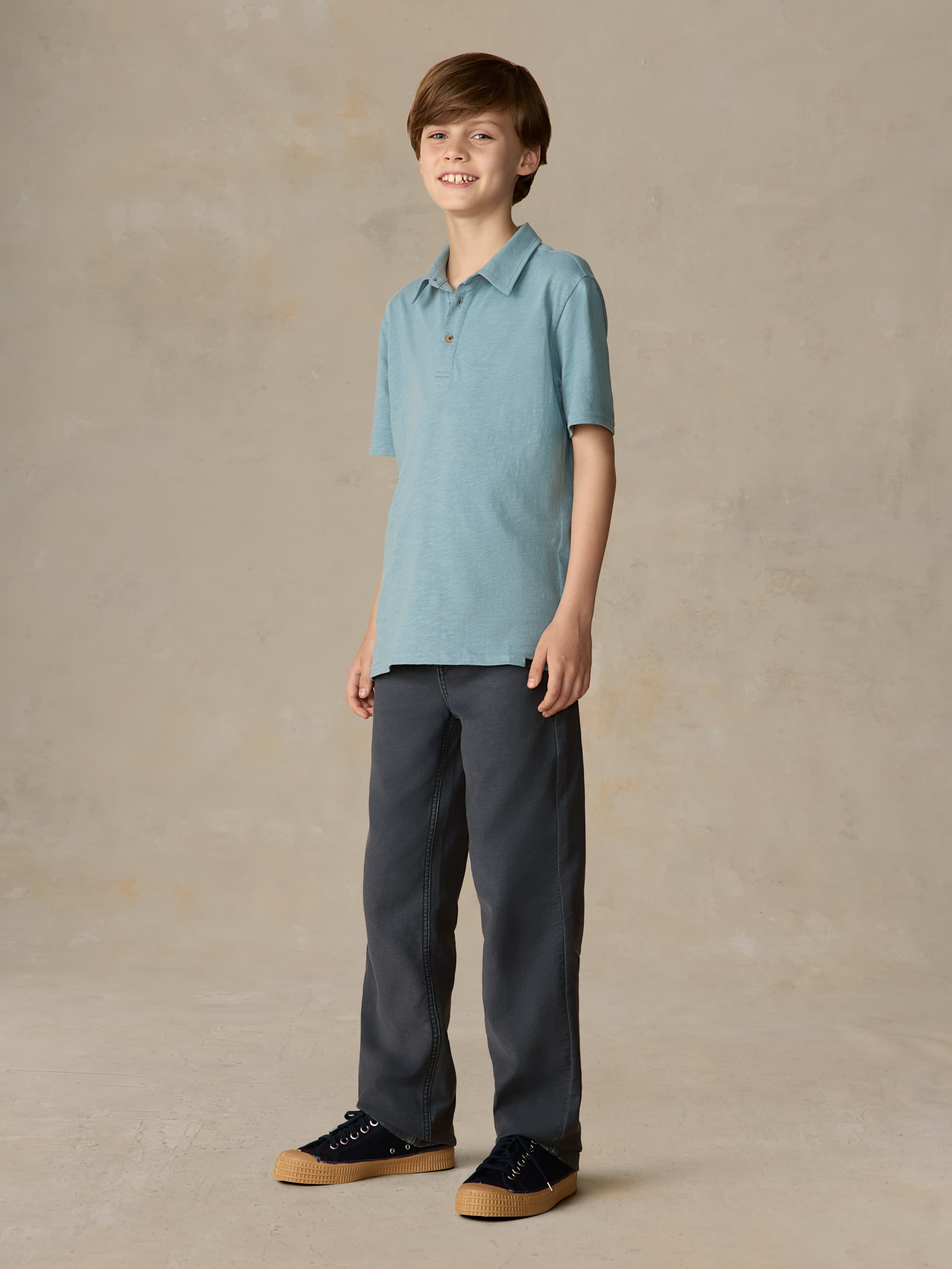 Child wearing a light blue polo and navy pants against a beige background