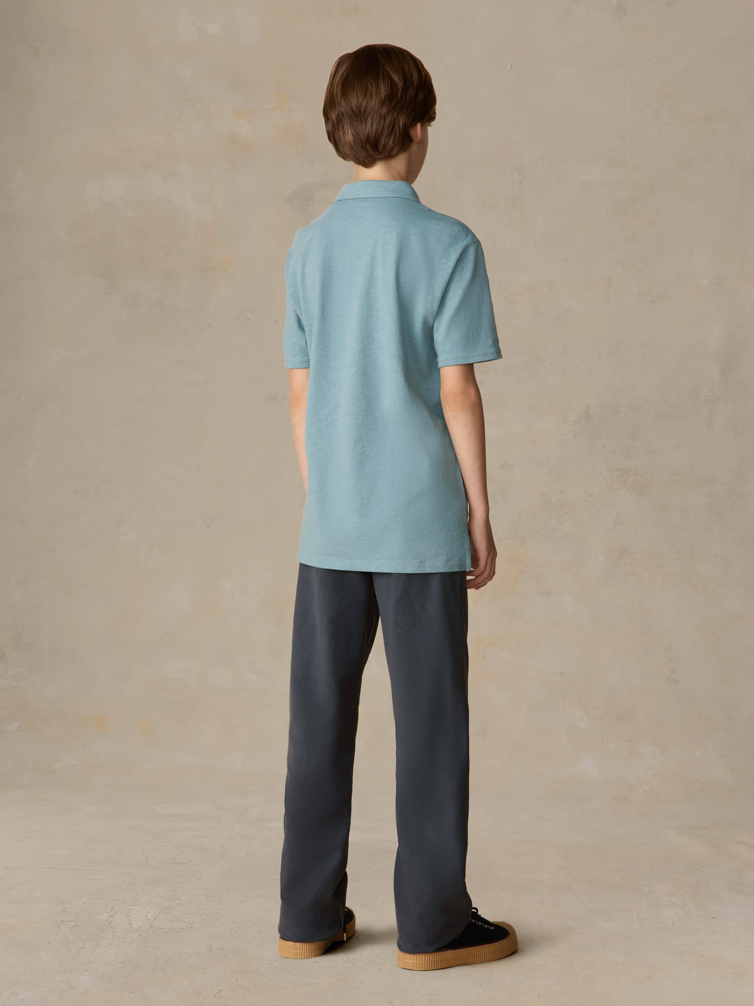 Child wearing a light blue polo and navy pants against a beige background