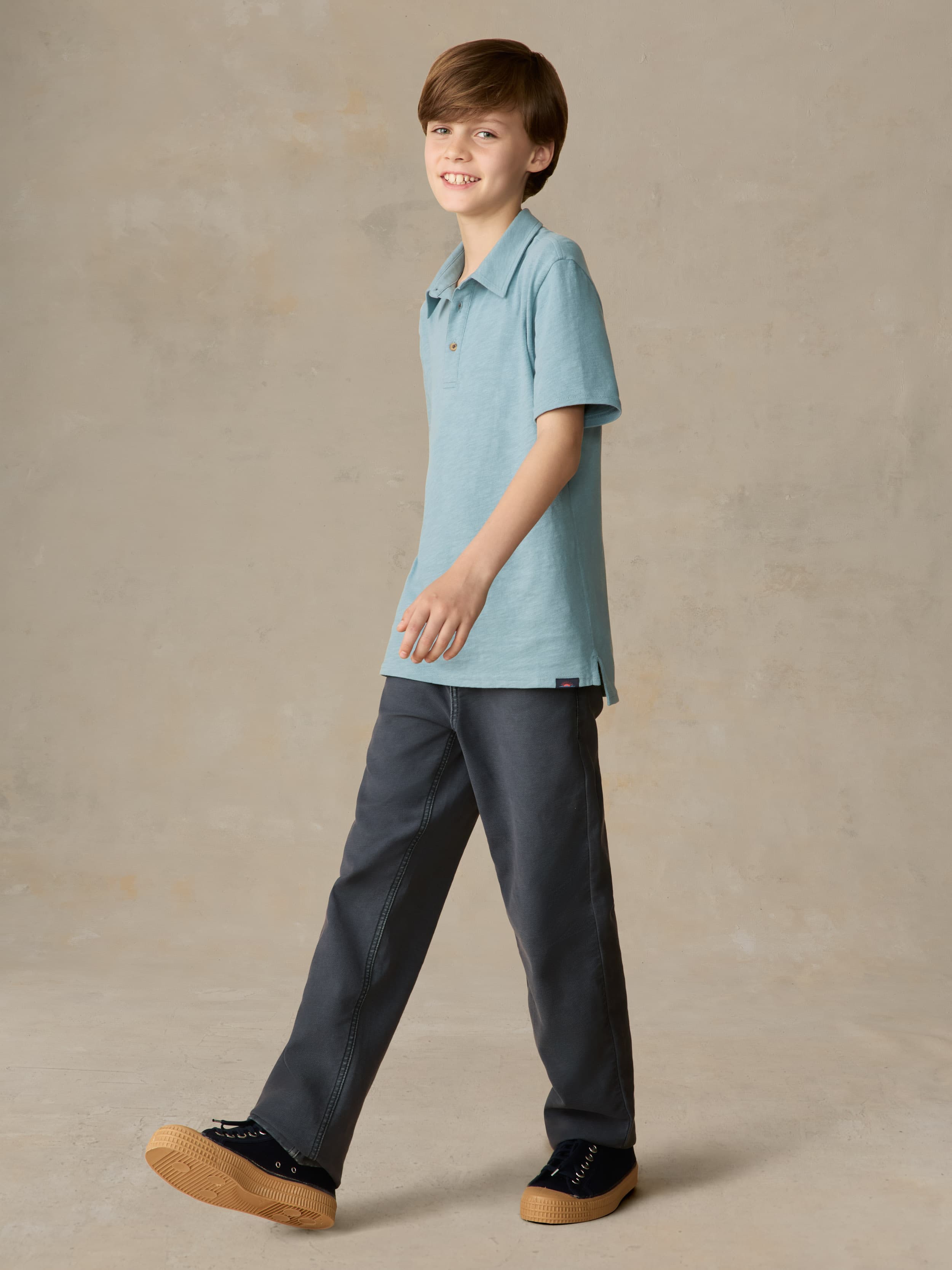 Child wearing a light blue polo and navy pants against a beige background