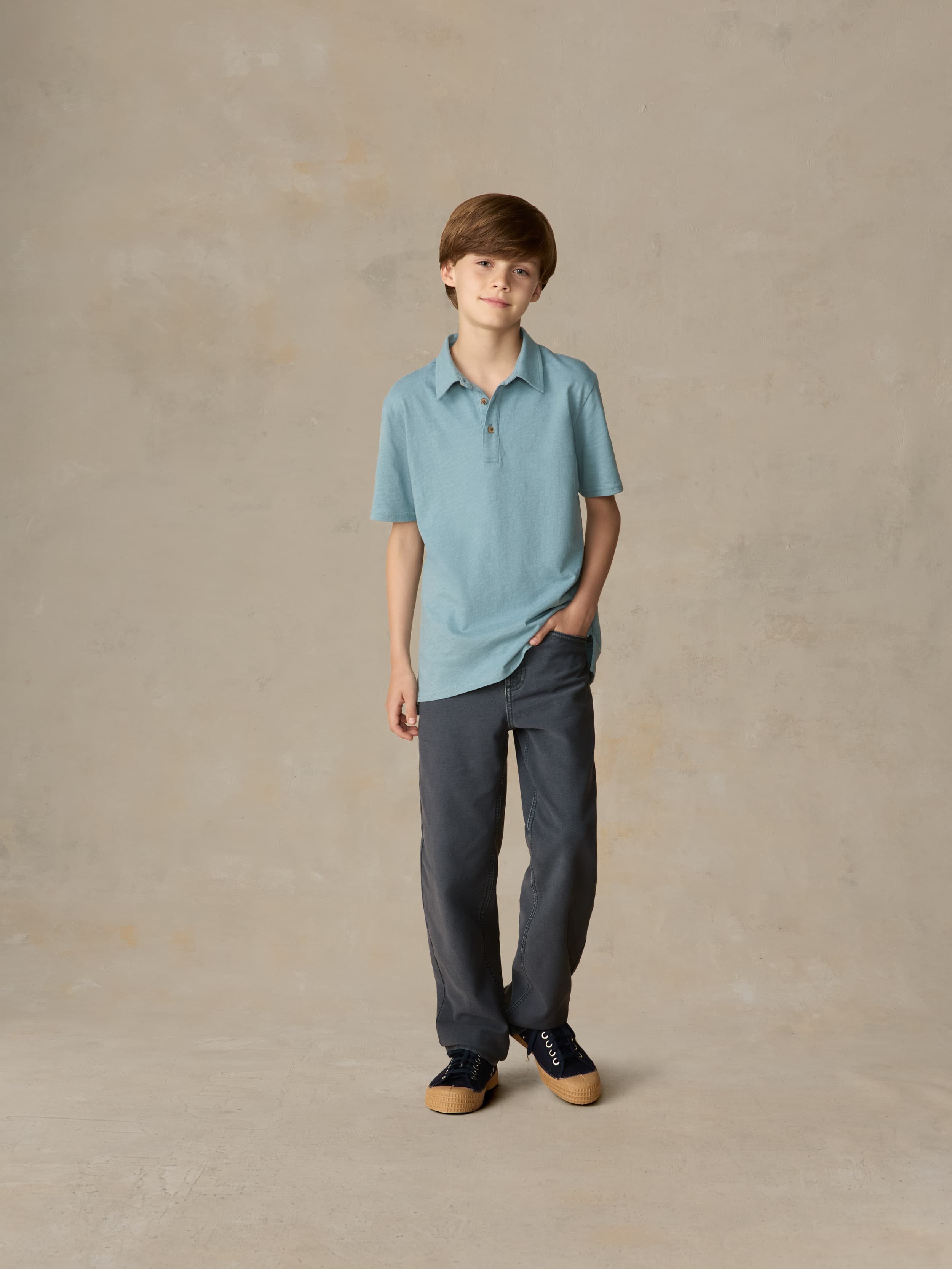 Child wearing a light blue polo and navy pants against a beige background