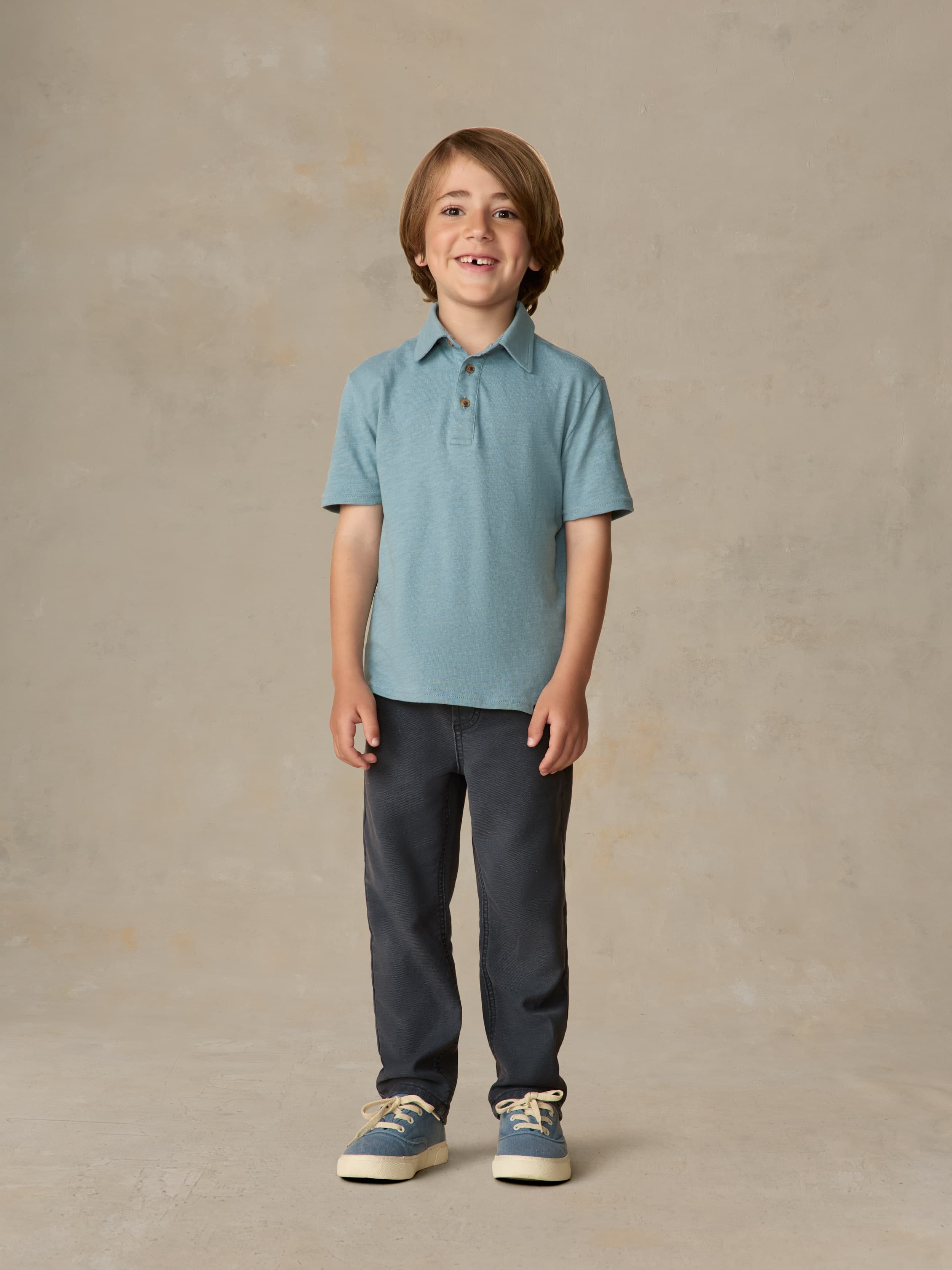 Child wearing a light blue polo shirt and navy pants against a beige background