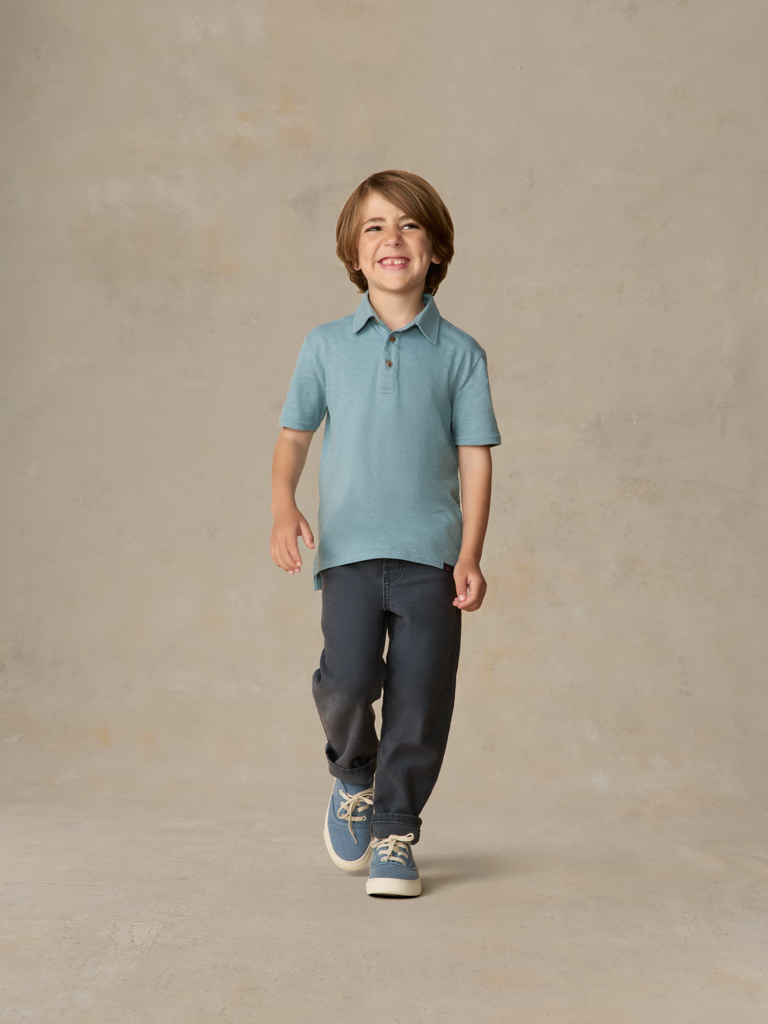 Child wearing a light blue polo shirt and navy pants against a beige background