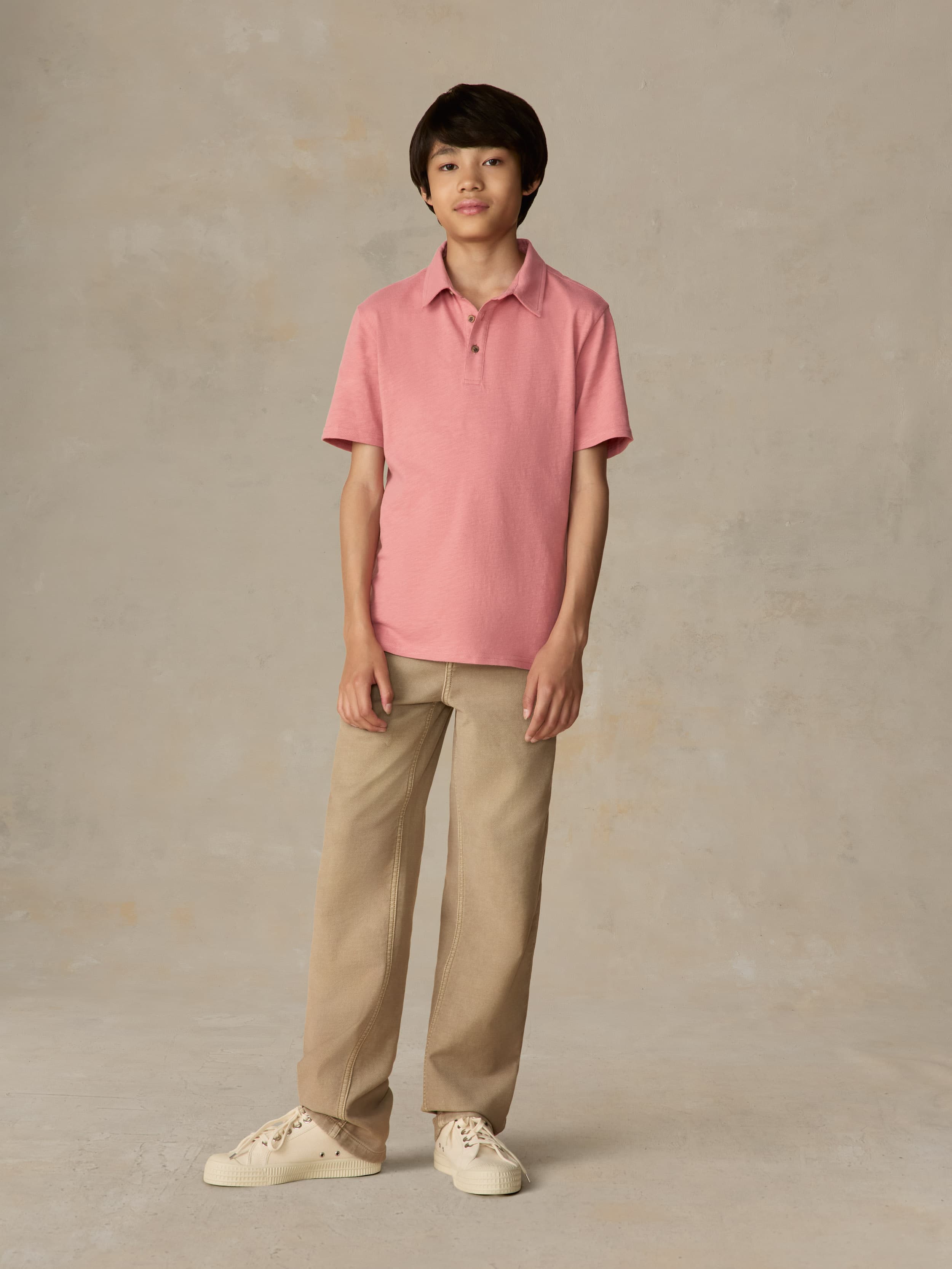 Child wearing a red polo shirt and beige pants against a beige background