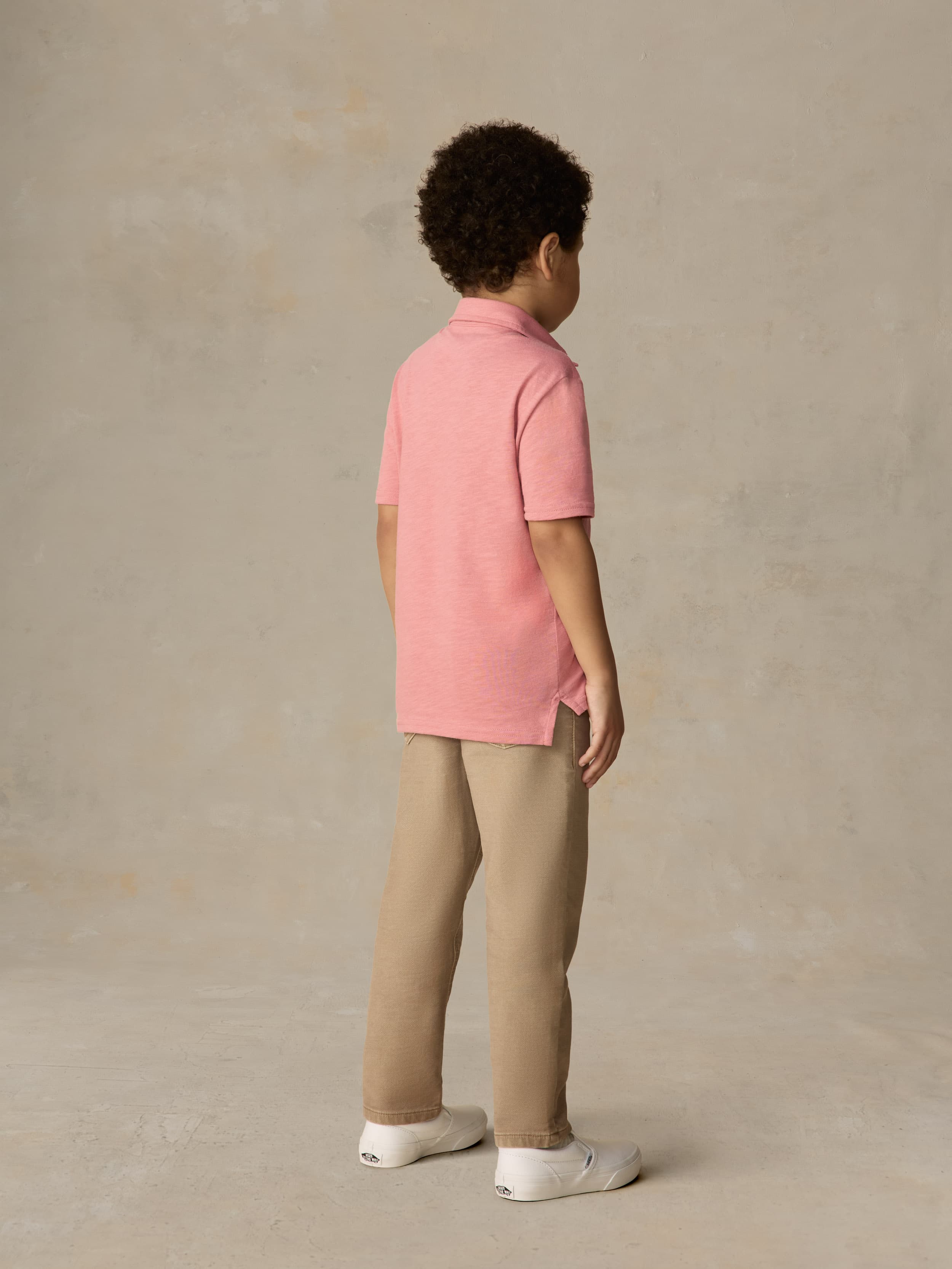 Child wearing a red polo shirt and beige pants against a beige background