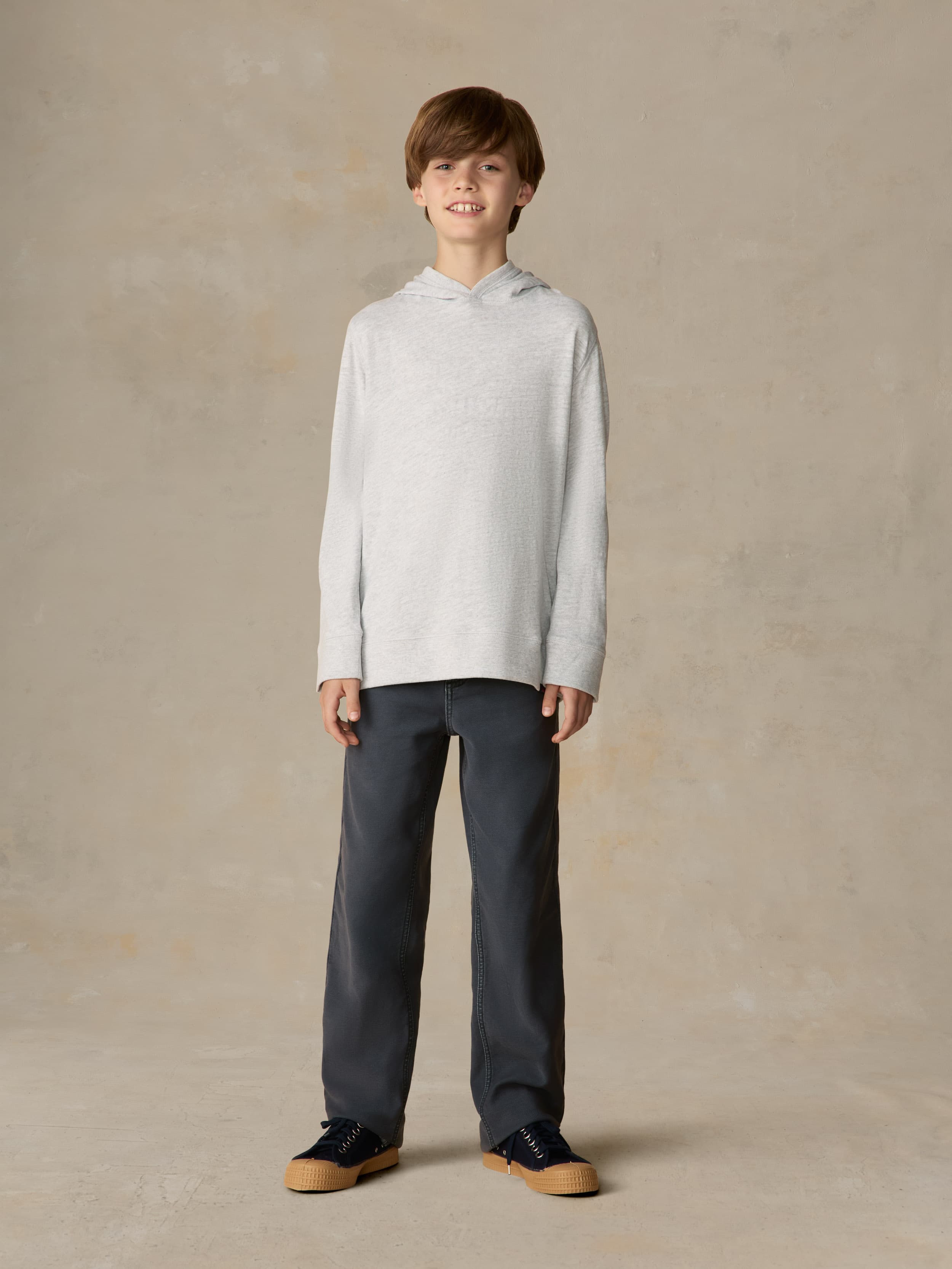 Child wearing a grey hoodie and navy pants against a beige background
