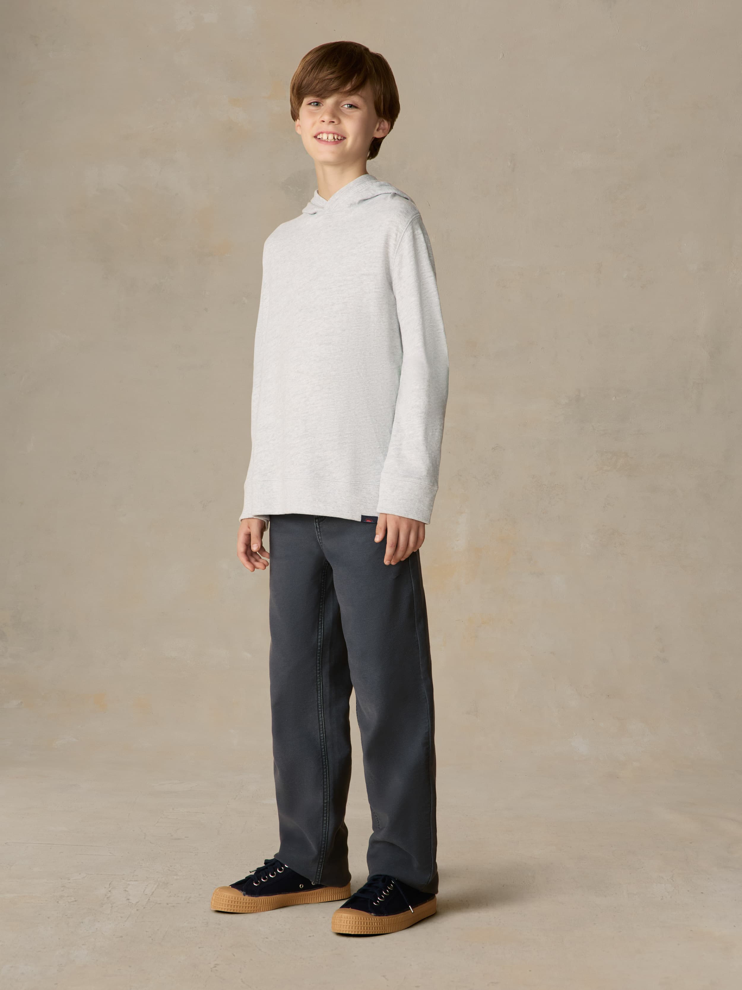 Child wearing a grey hoodie and navy pants against a beige background