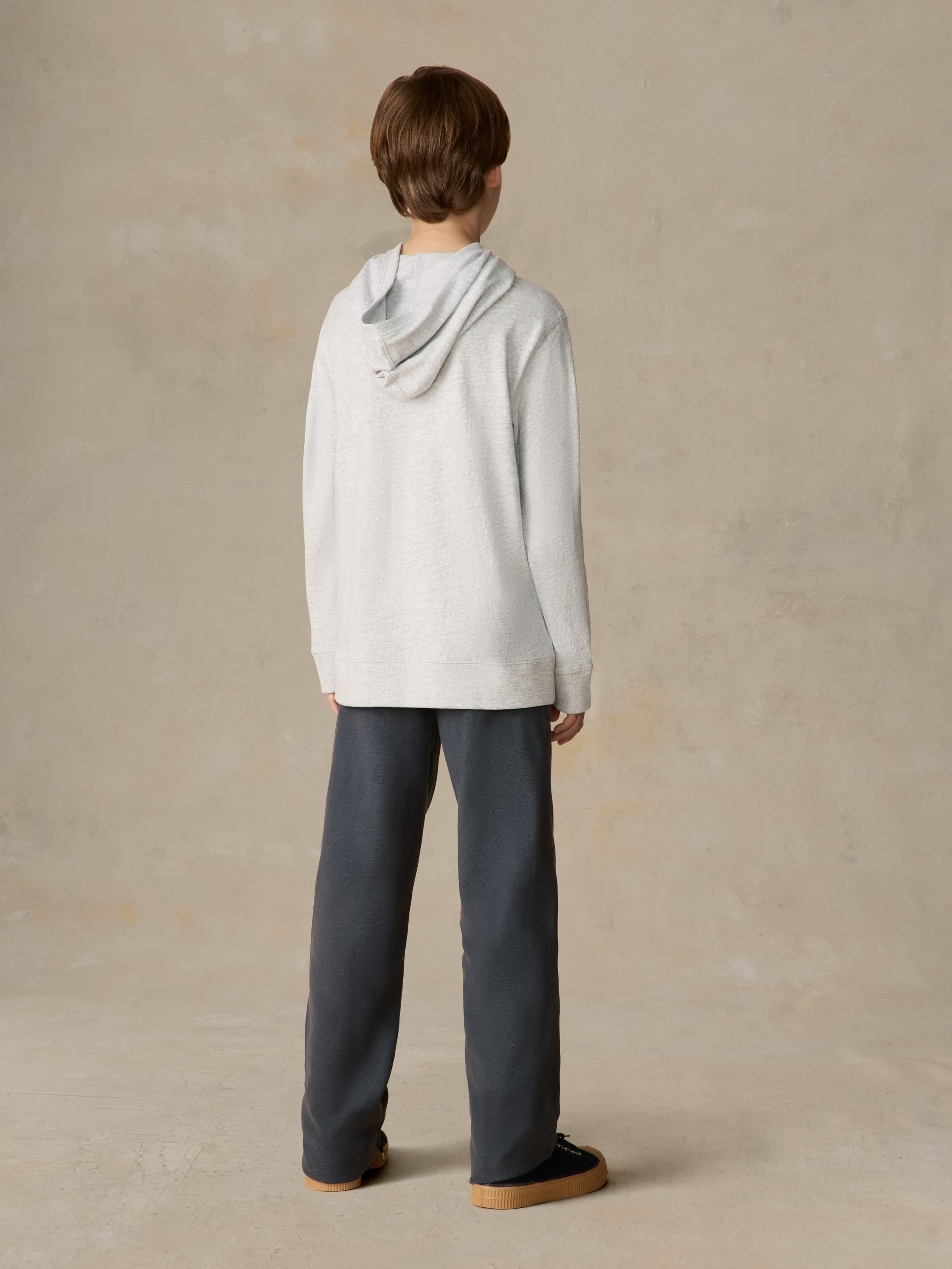 Child wearing a grey hoodie and navy pants against a beige background