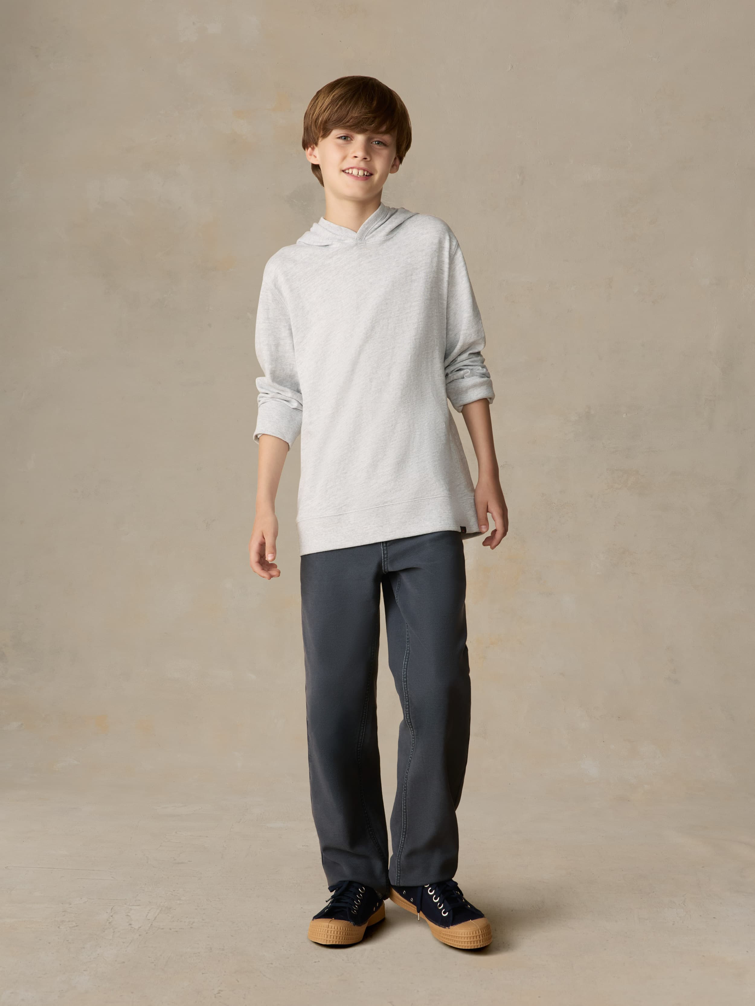 Child wearing a grey hoodie and navy pants against a beige background