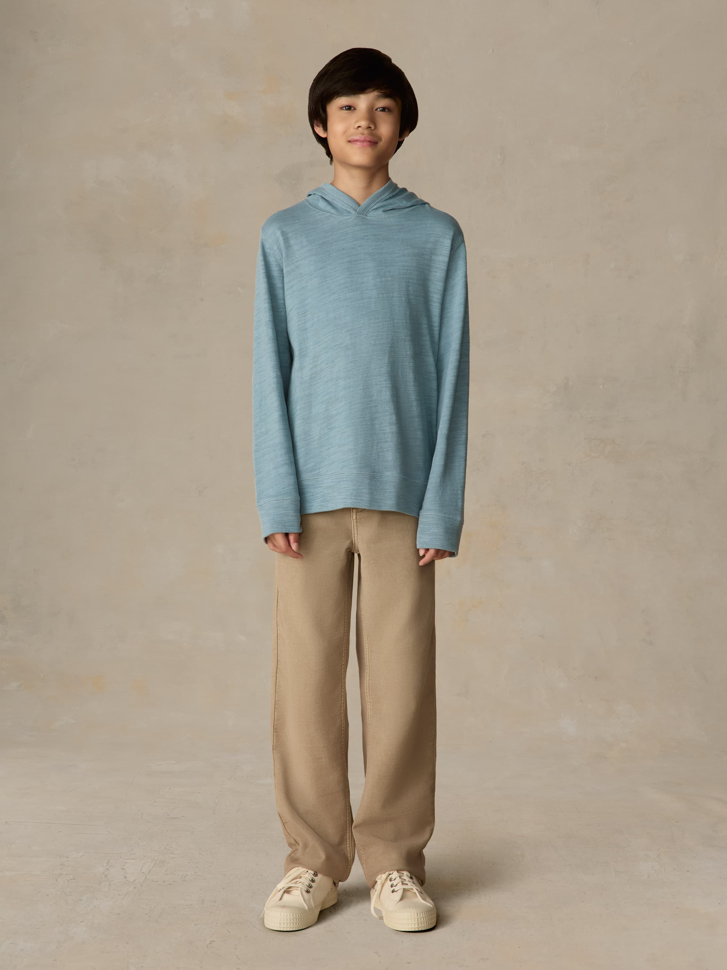 Child wearing a light blue hoodie and beige pants against a beige background