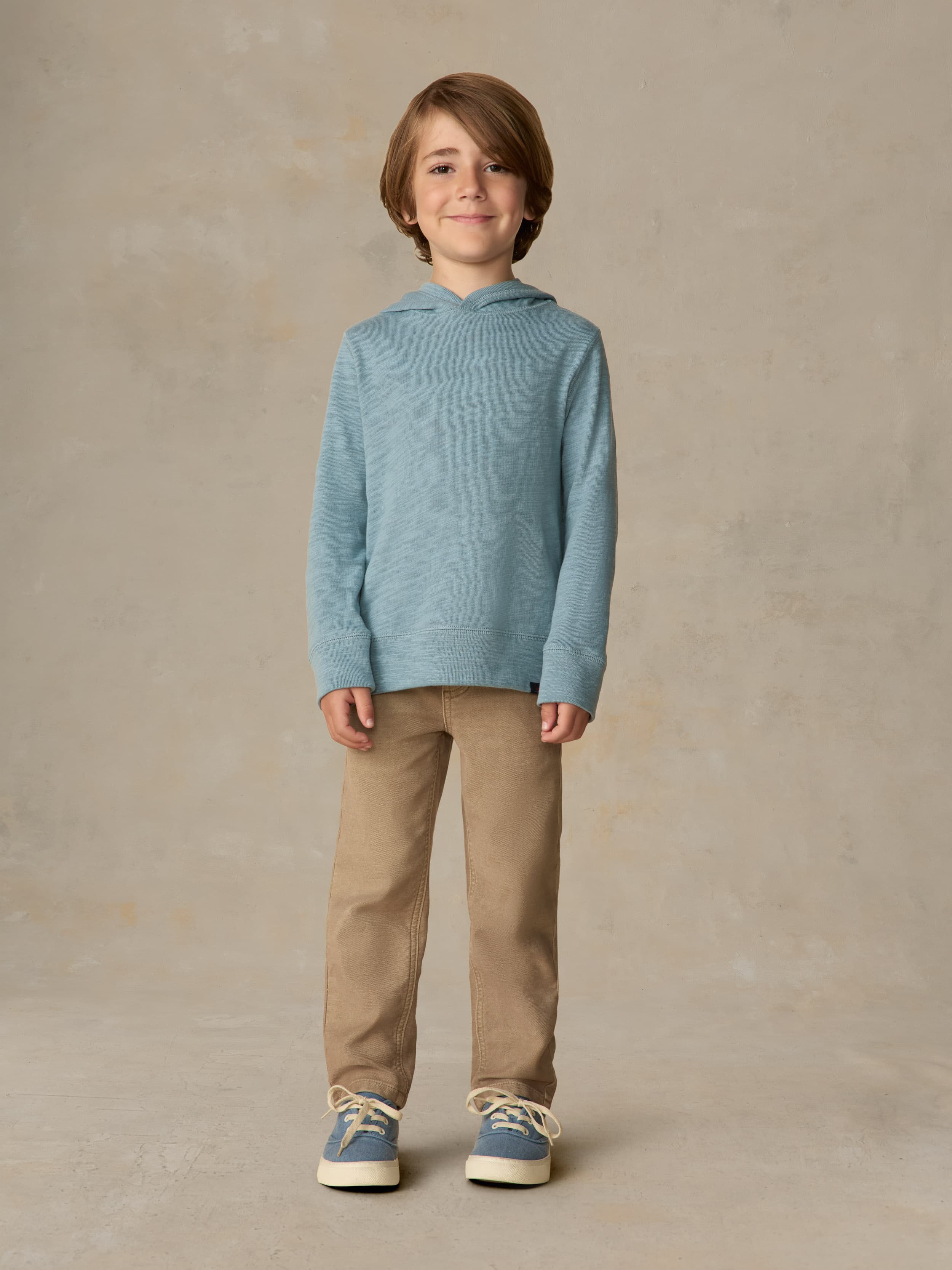 Child wearing a light blue hoodie and beige pants against a beige background