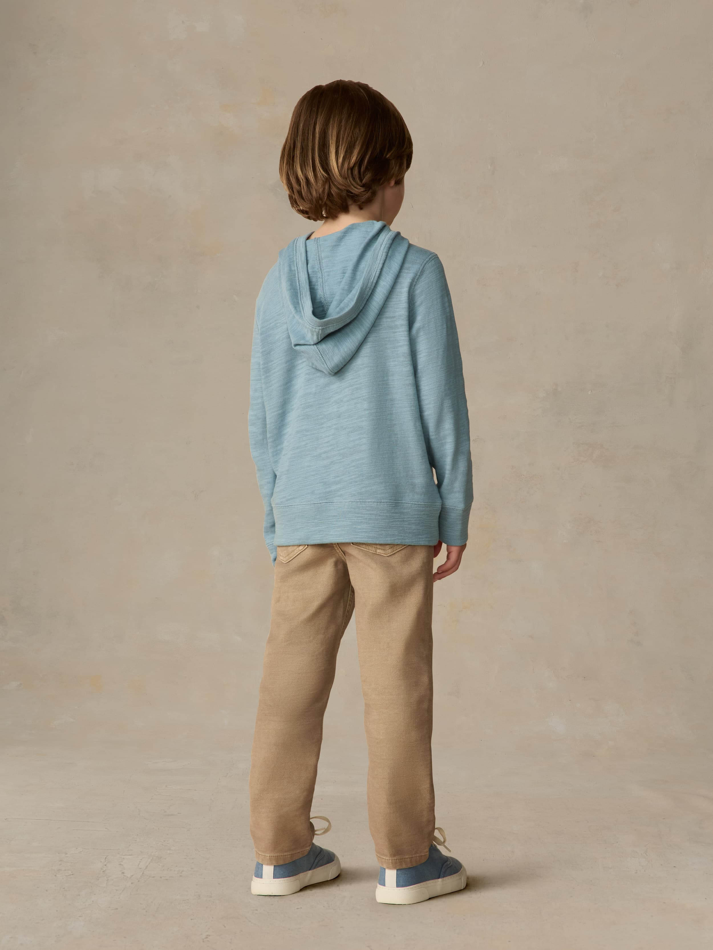 Child wearing a light blue hoodie and beige pants against a beige background