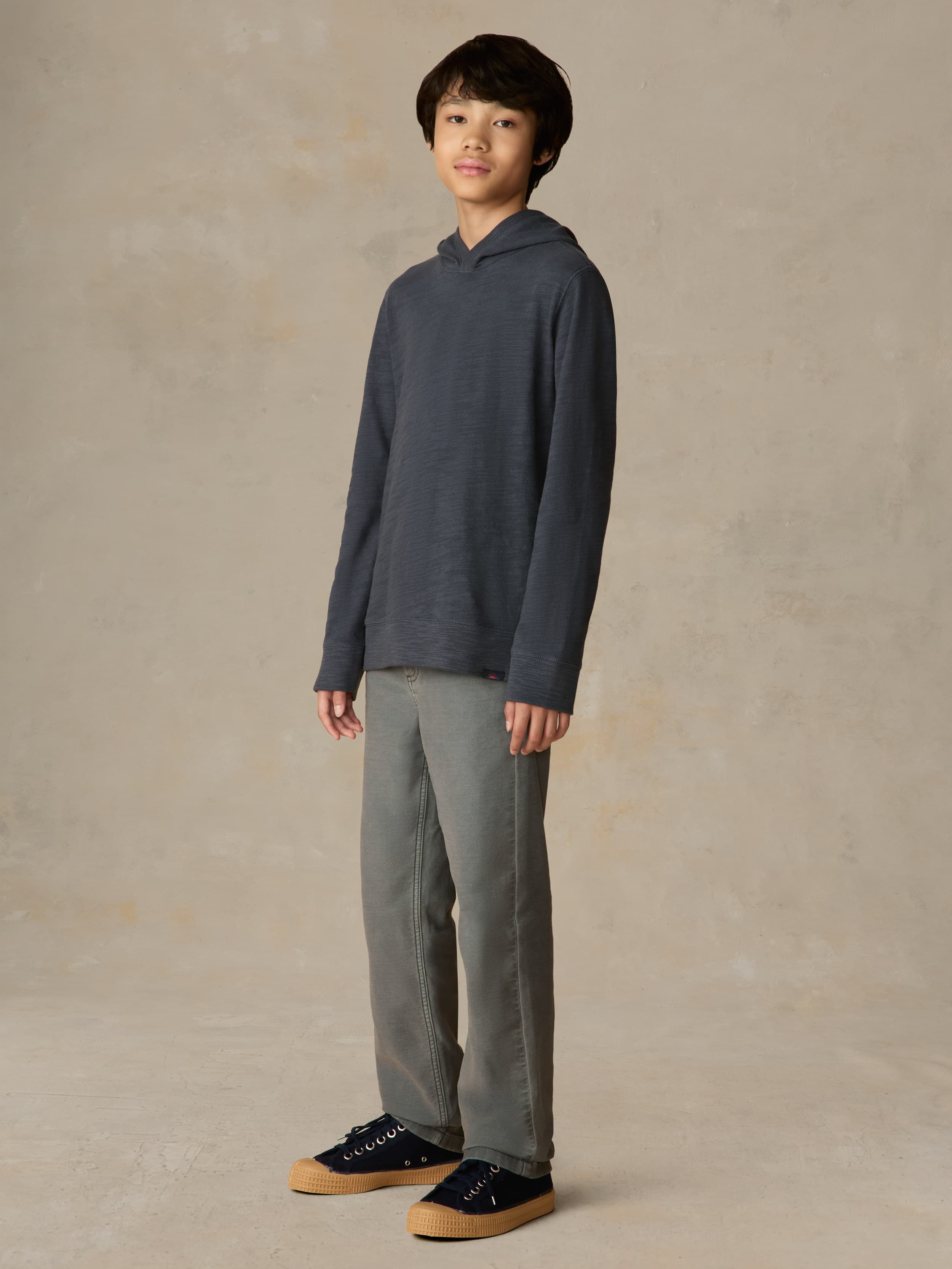 Child wearing a navy hoodie and grey pants against a beige background