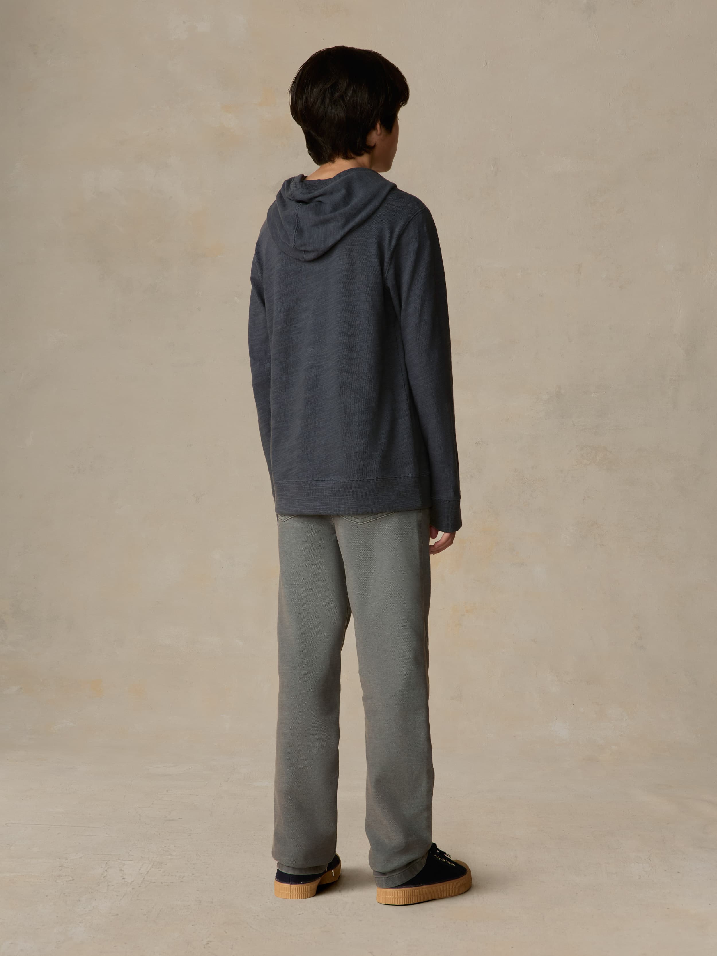 Child wearing a navy hoodie and grey pants against a beige background