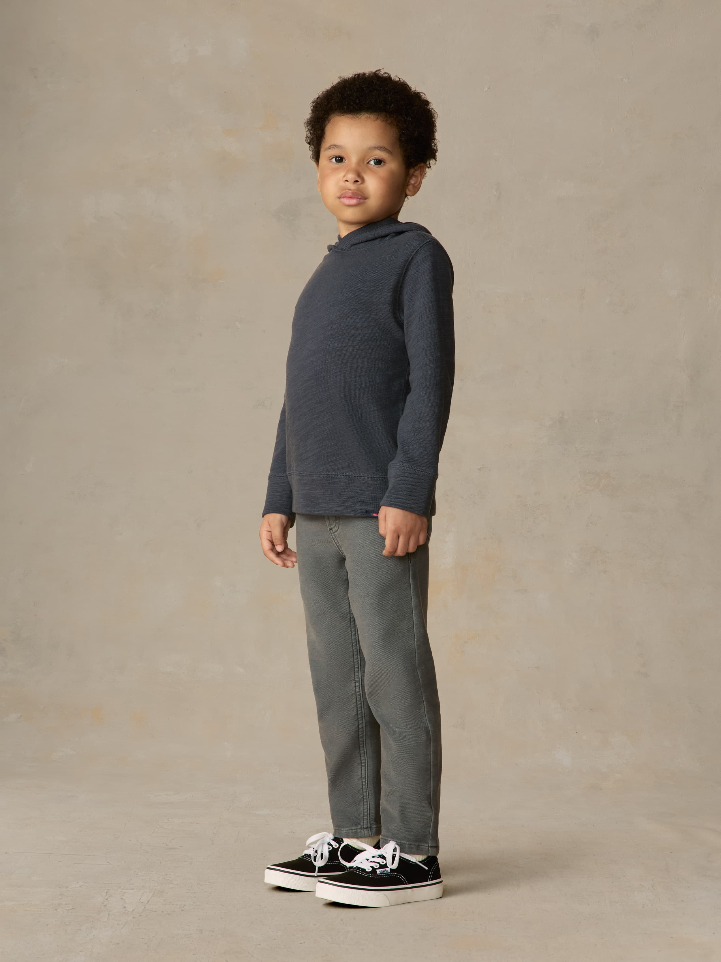 Child wearing a navy hoodie and grey pants against a beige background