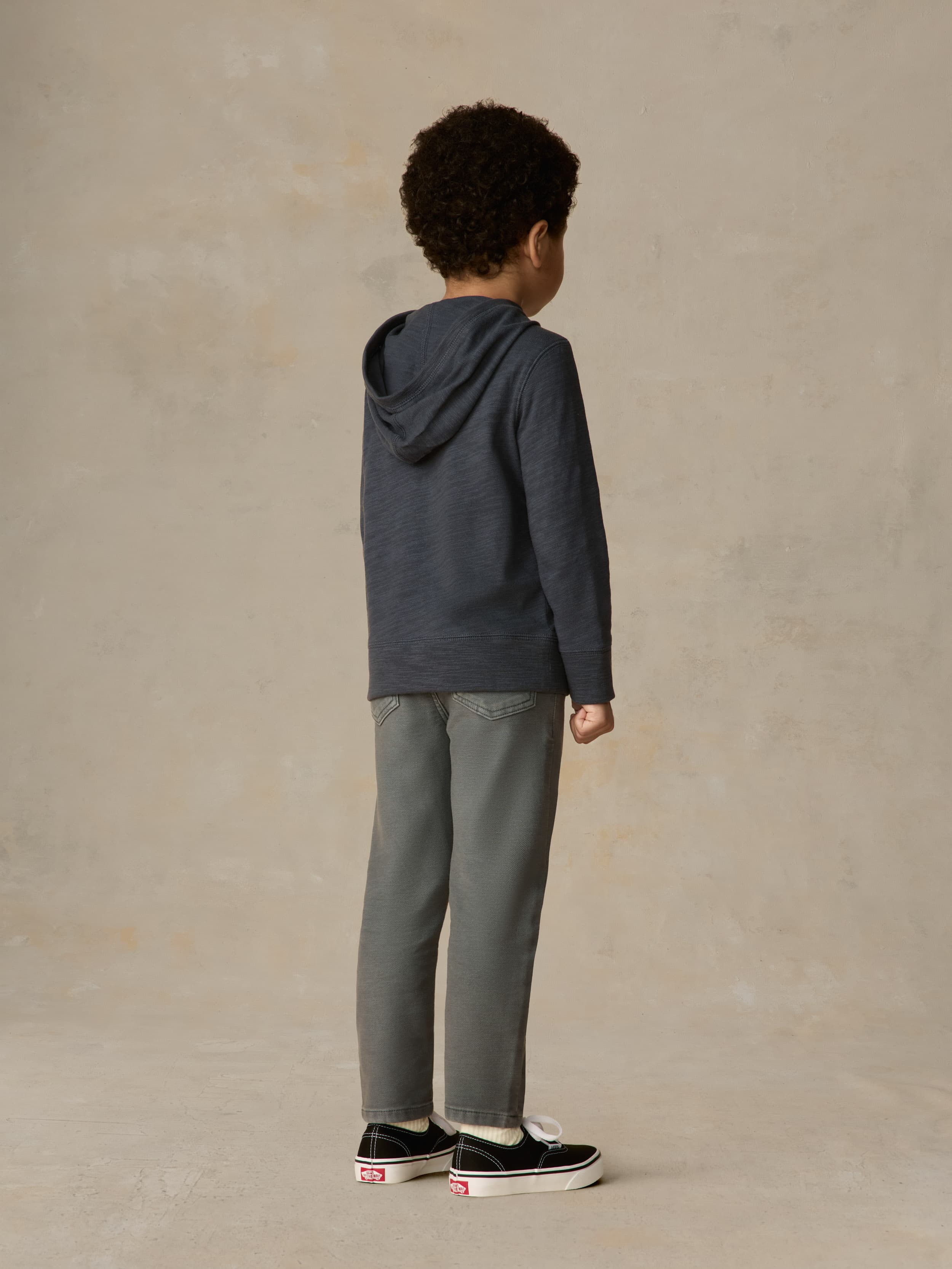Child wearing a navy hoodie and grey pants against a beige background