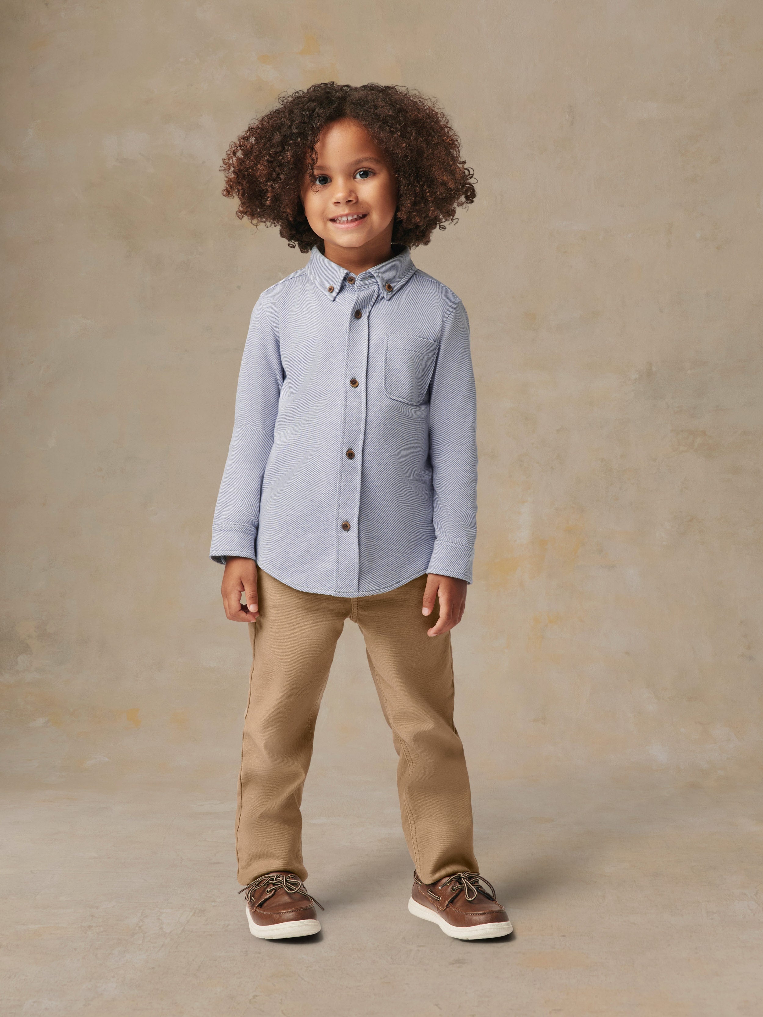 A child wearing a blue button up shirt and beige pants