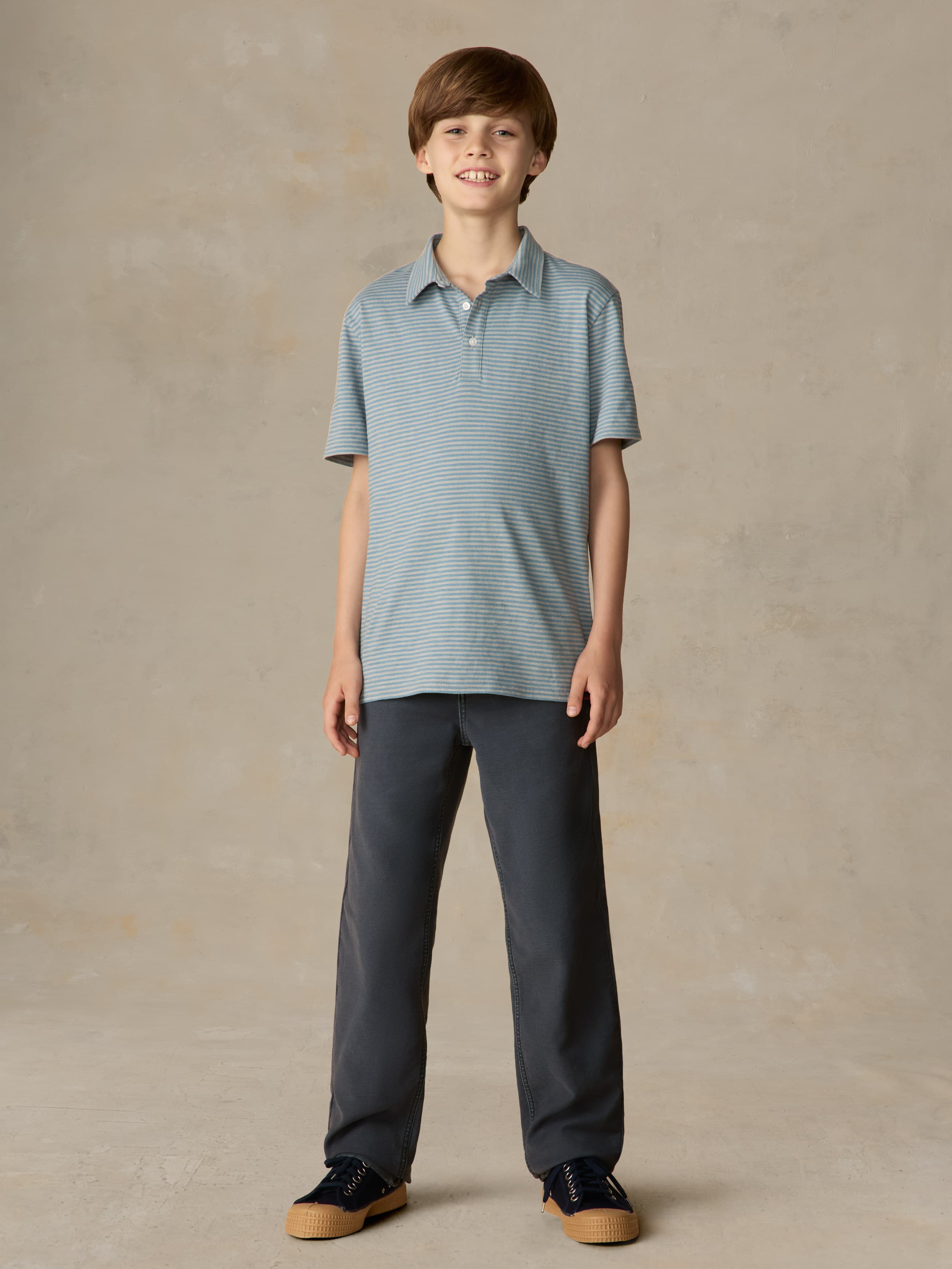 Child wearing a blue striped polo and navy pants against a beige background