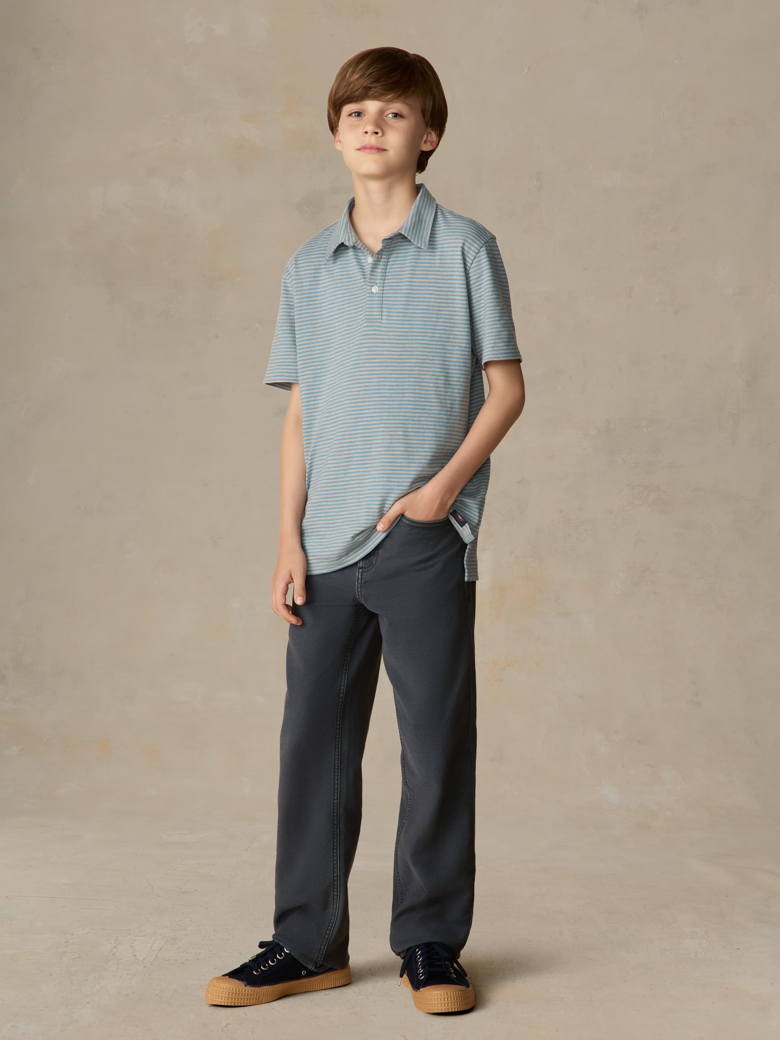 Child wearing a blue striped polo and navy pants against a beige background