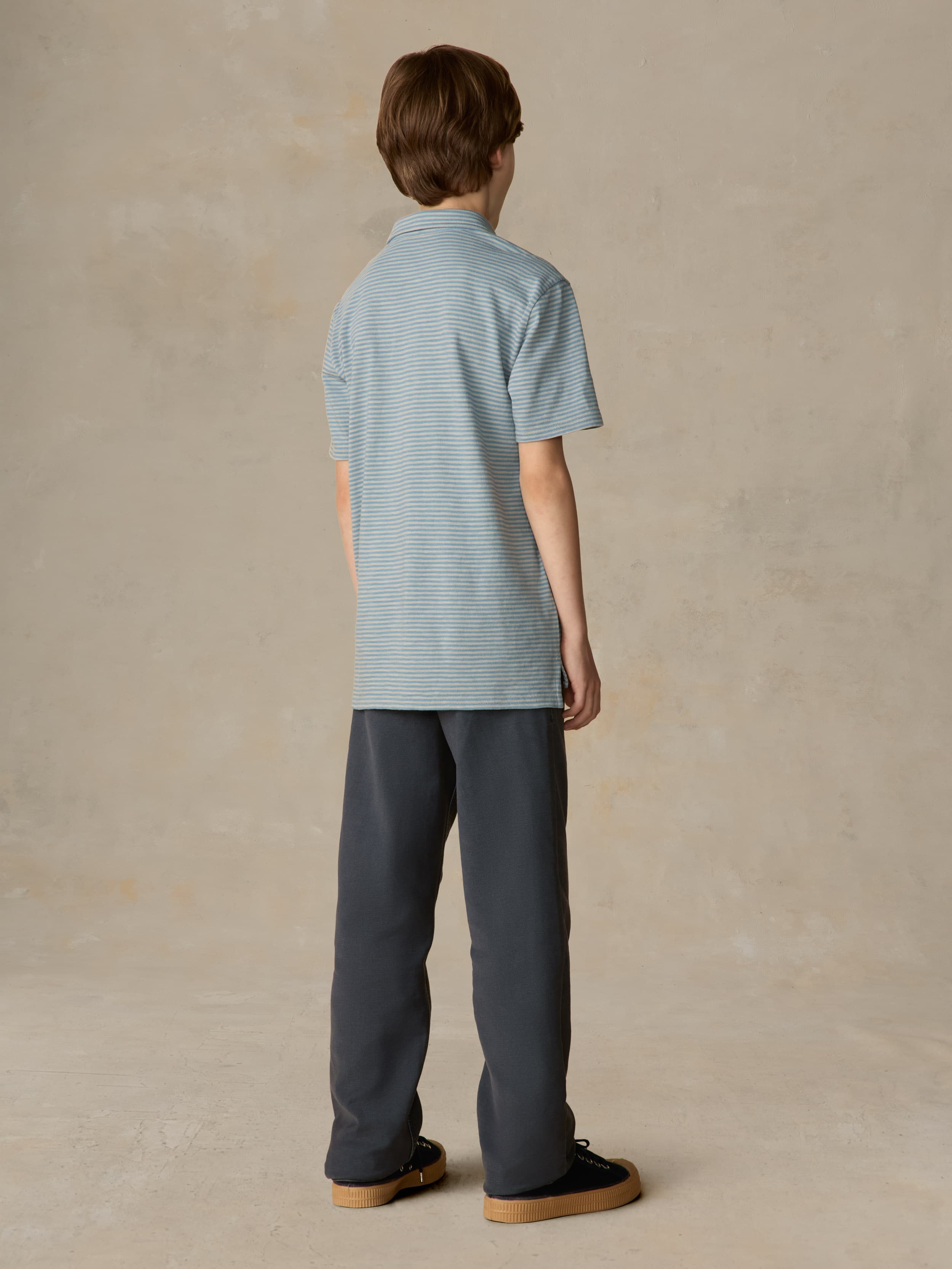 Child wearing a blue striped polo and navy pants against a beige background