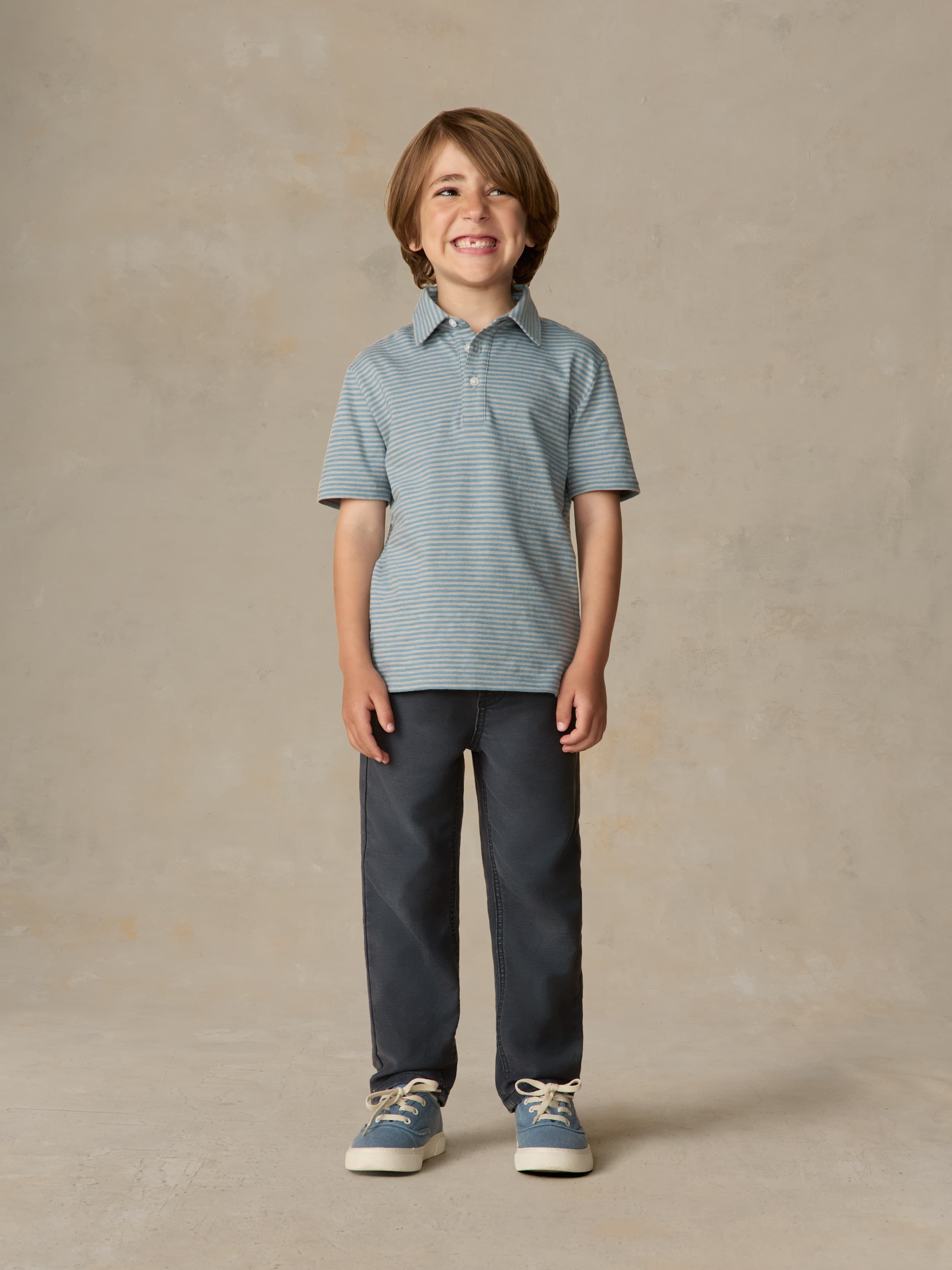 Child wearing a blue striped polo and navy pants against a beige background