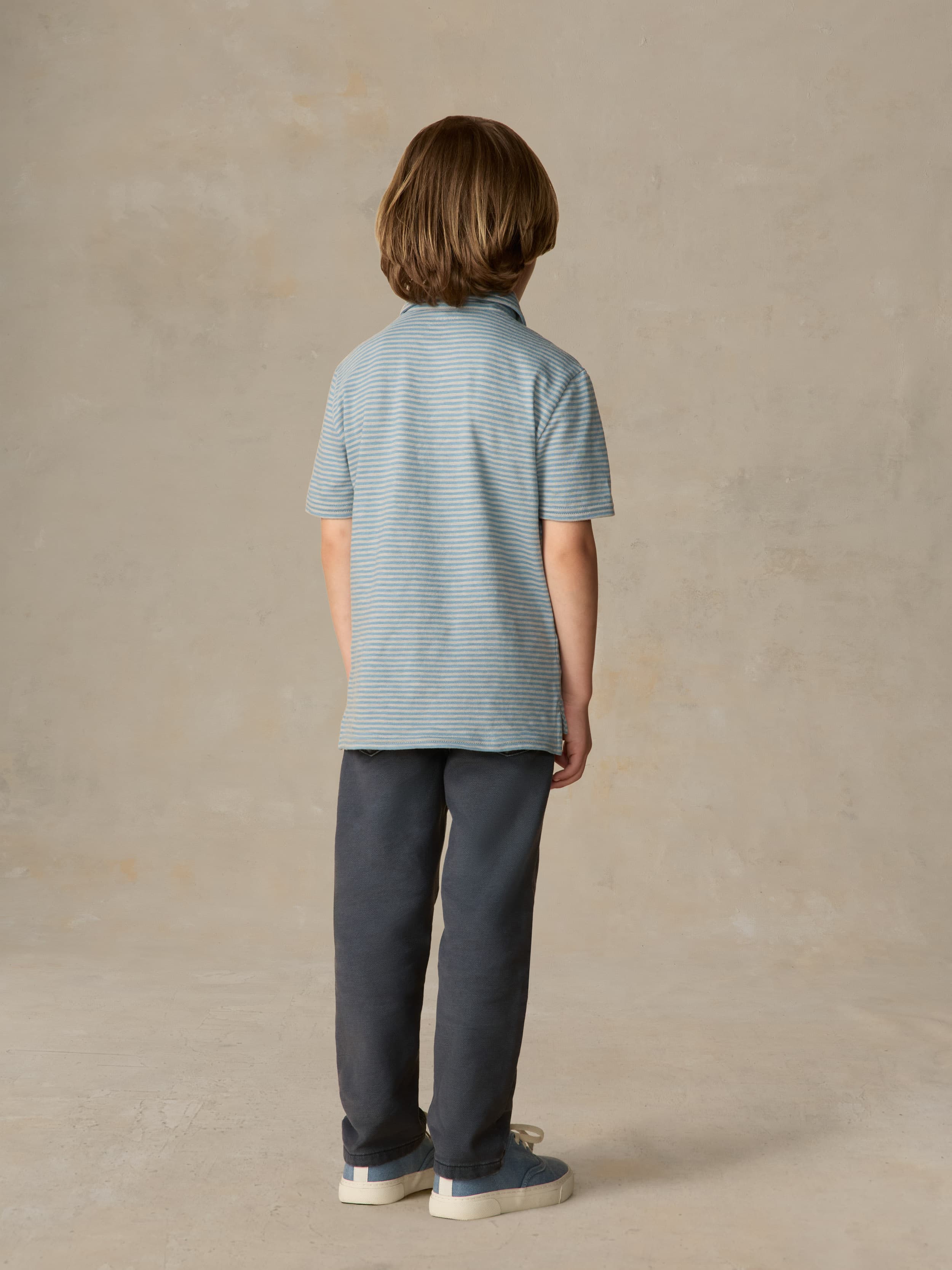Child wearing a blue striped polo and navy pants against a beige background