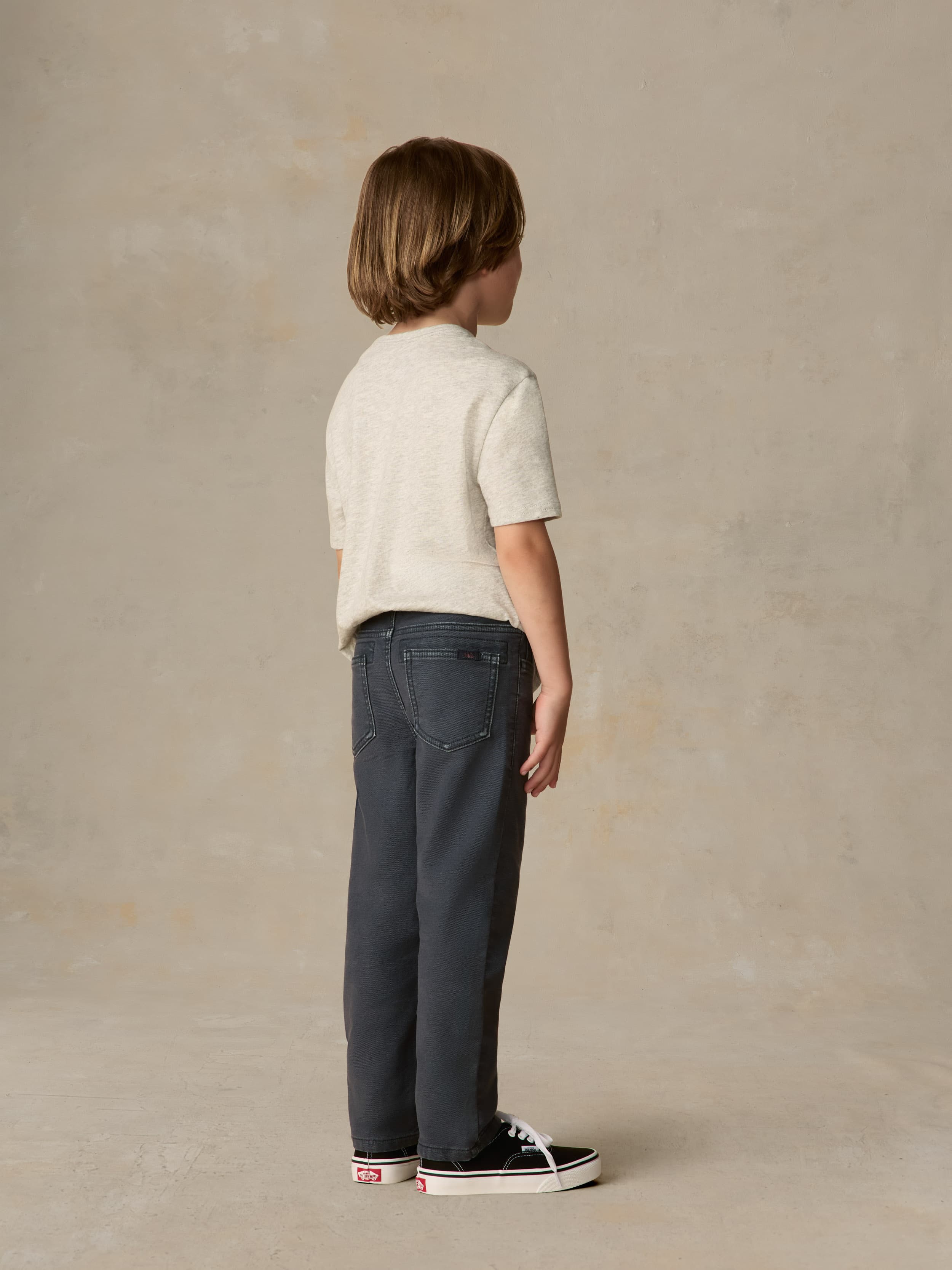 Child wearing graphic grey tee and navy pants against a beige background