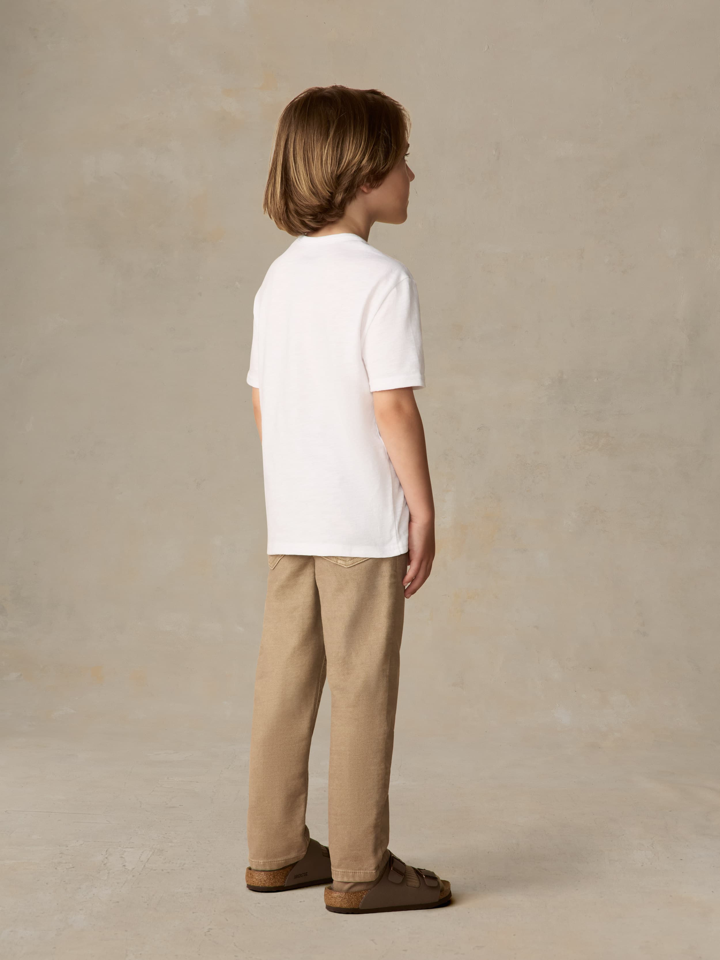 Child wearing a white shirt and beige pants against a beige background