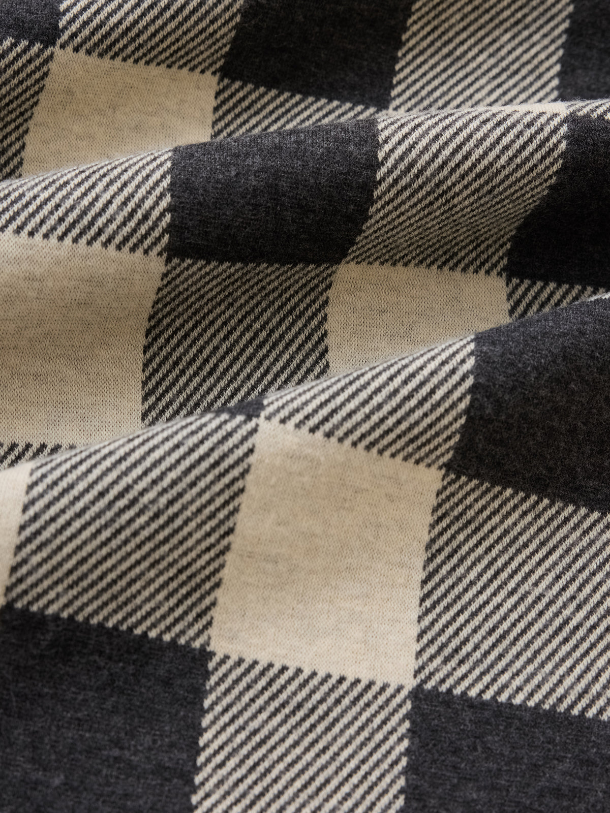 A close-up of a buffalo plaid fabric with large checkers in black and warm cream, showing the woven texture and folds., image 2 of 3