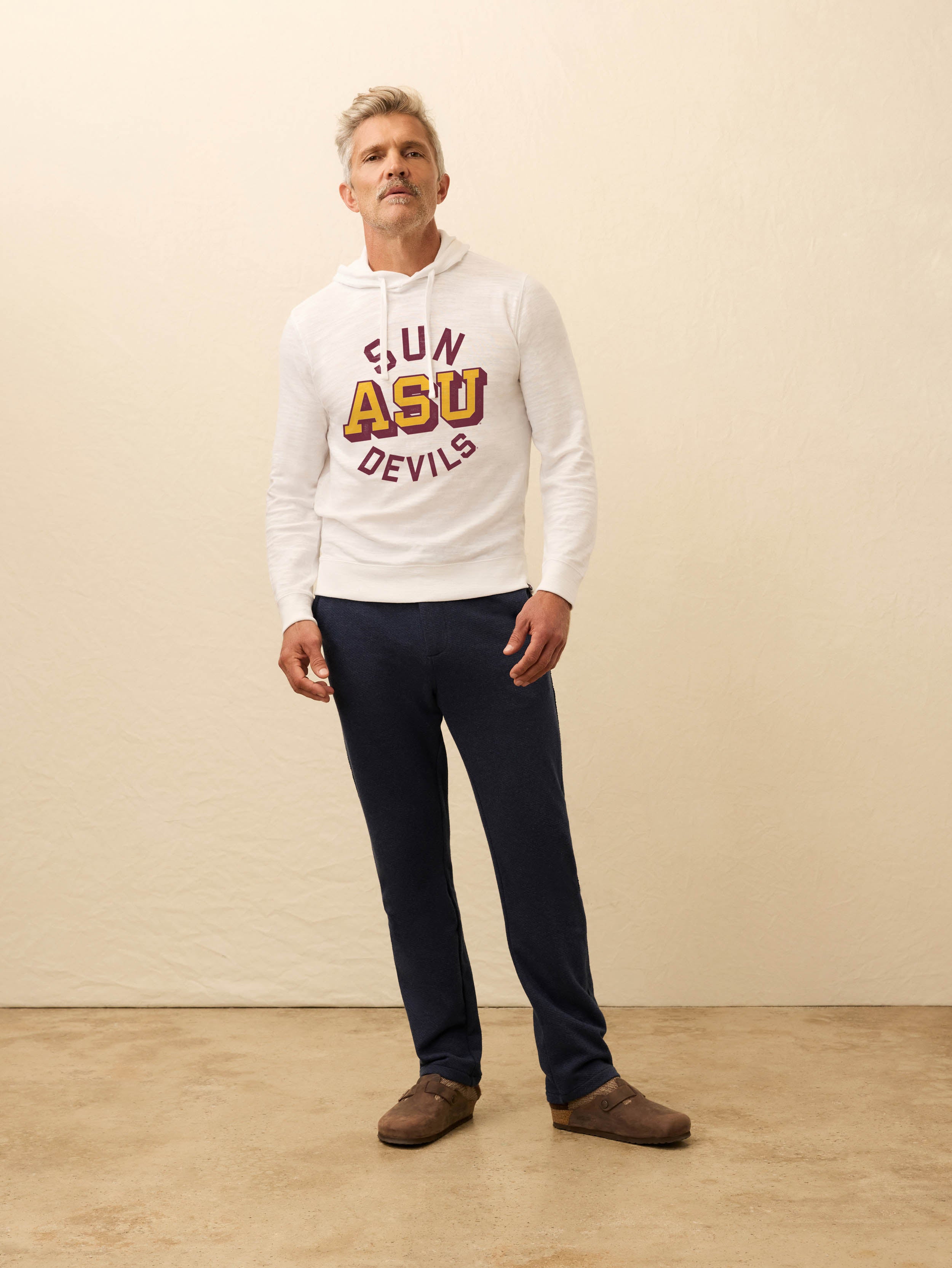 Man wearing a white hoodie with ASU graphic at the center front against a beige background
