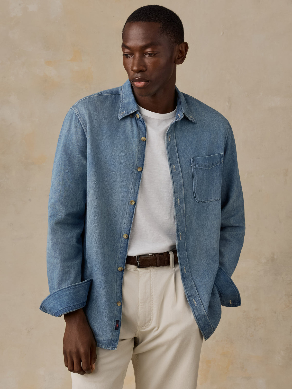 Man wearing a light blue denim shirt against a beige background, image 1 of 5
