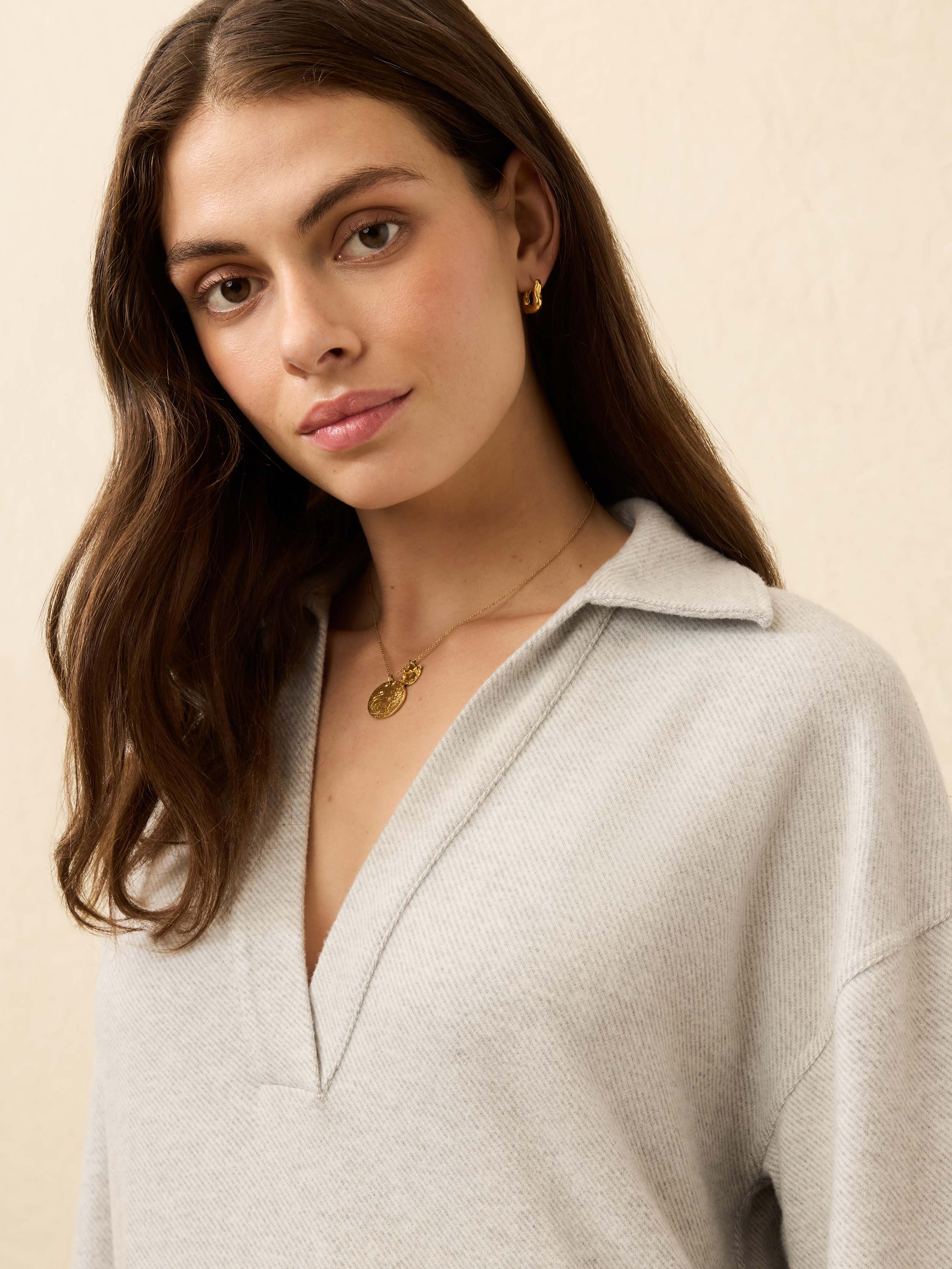 Woman is wearing grey sweater dress against a beige background