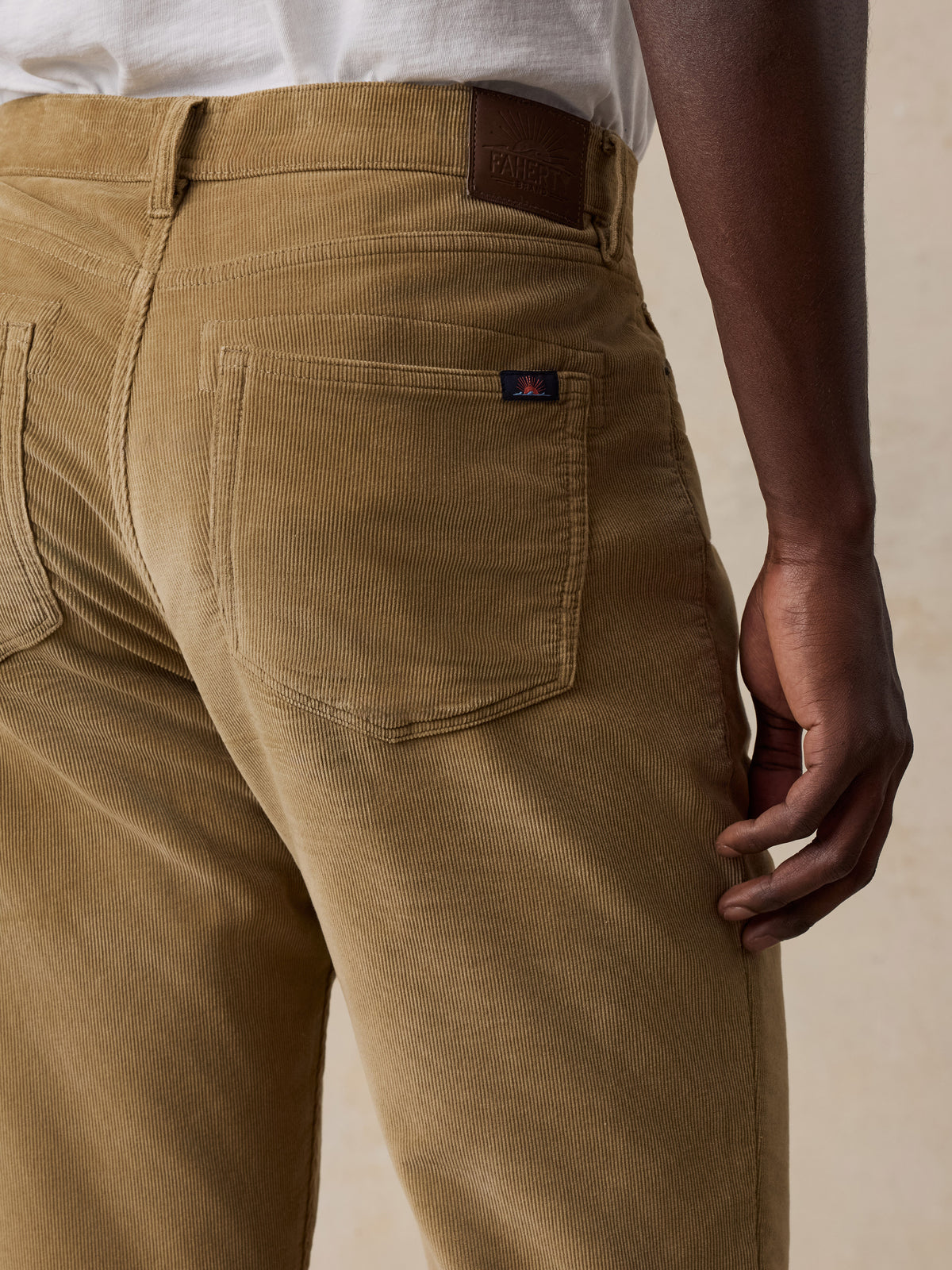 Close up of a man viewed from behind wearing a white tee and tan corduroy pants, image 5 of 5