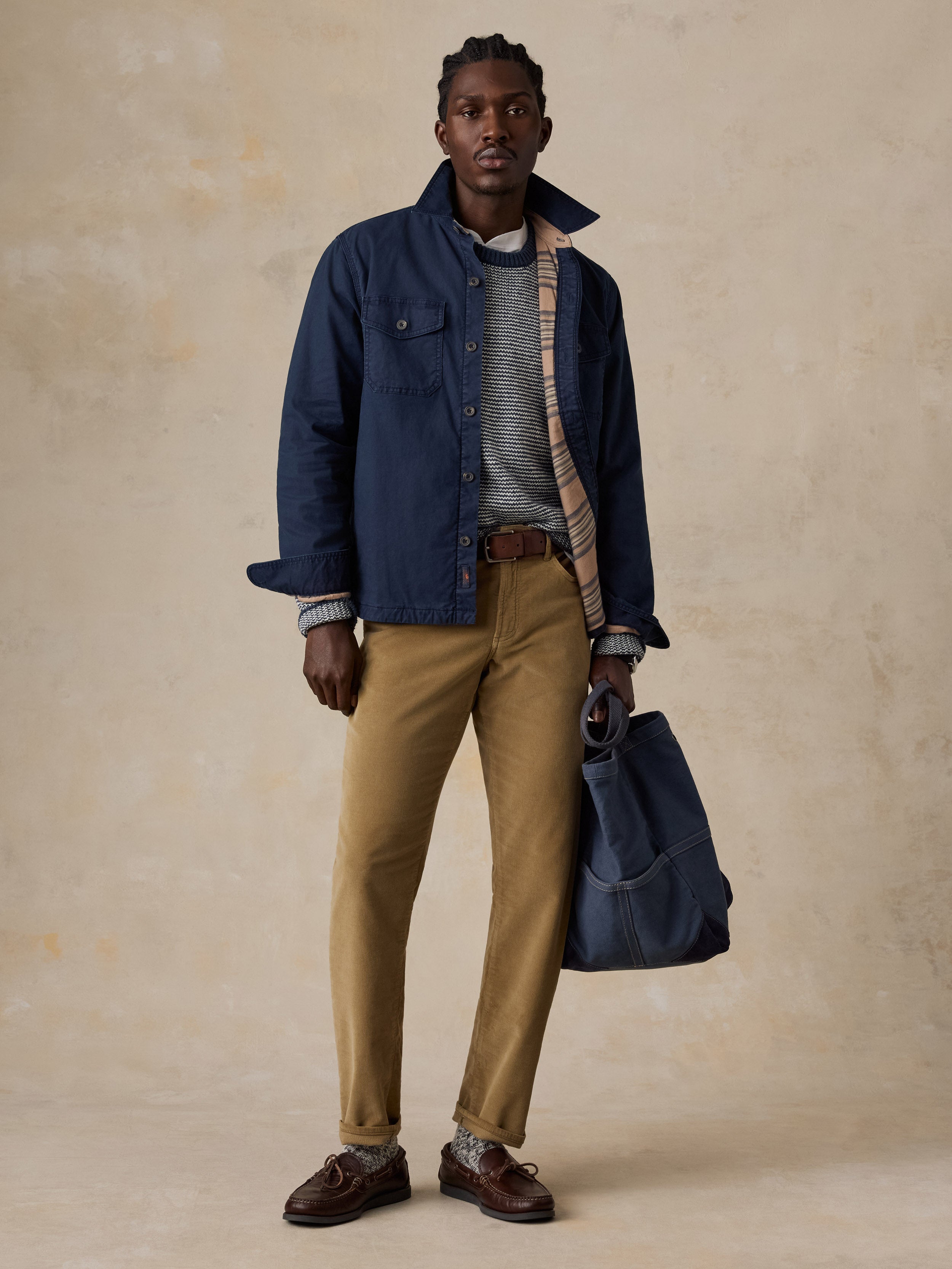 A man wearing a sweater, blue overshirt, and tan corduroy pants