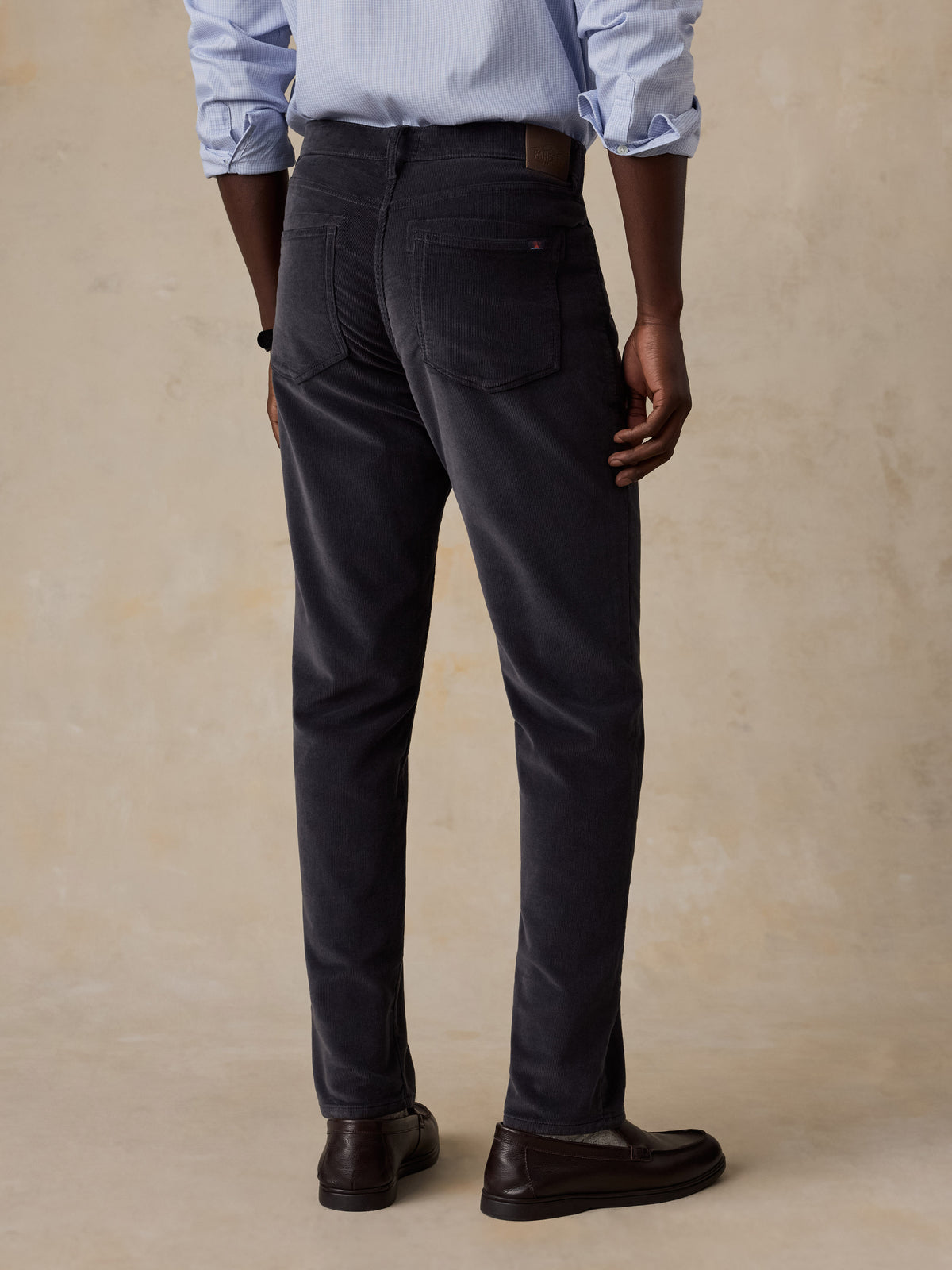A man viewed from behind wearing a blue button up shirt and grey corduroy pants, image 3 of 5