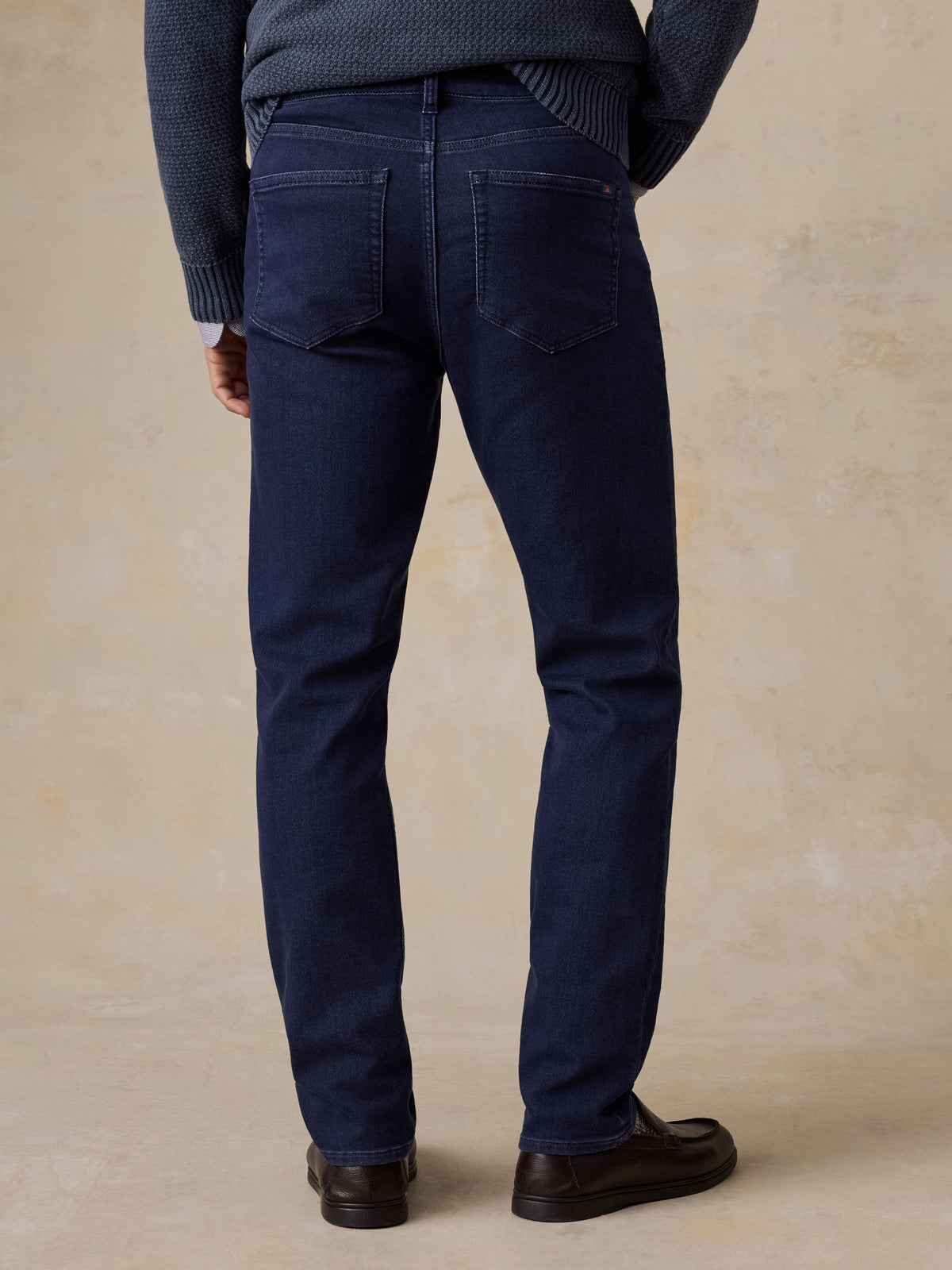 A man viewed from behind wearing a blue sweater, blue jeans, and black shoes, image 2 of 5